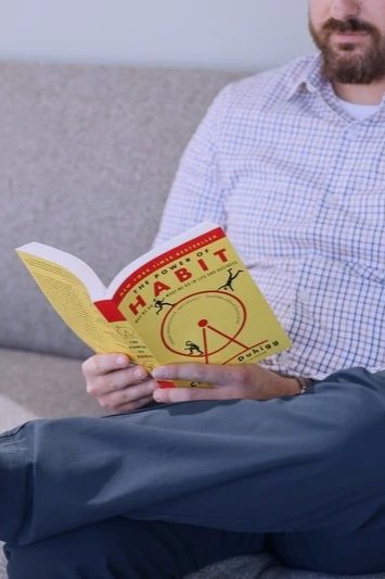 A man sitting outdoors on a bench, reading a book titled "Habits" with a circular chart on the cover. Evidenced based therapy practices being learned.