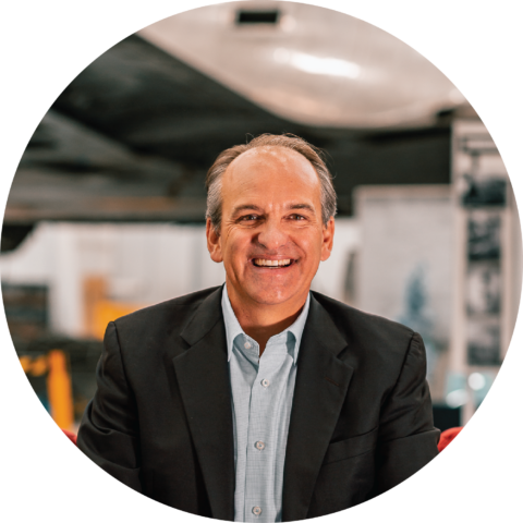 Michael Stoltzfus, smiling in a suit, standing in an aircraft hangar