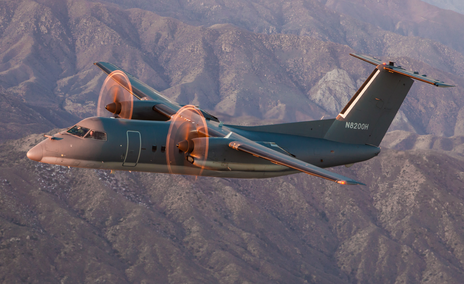 Small vintage propeller airplane on grassy field beside water with trees and cloudy sky in background.