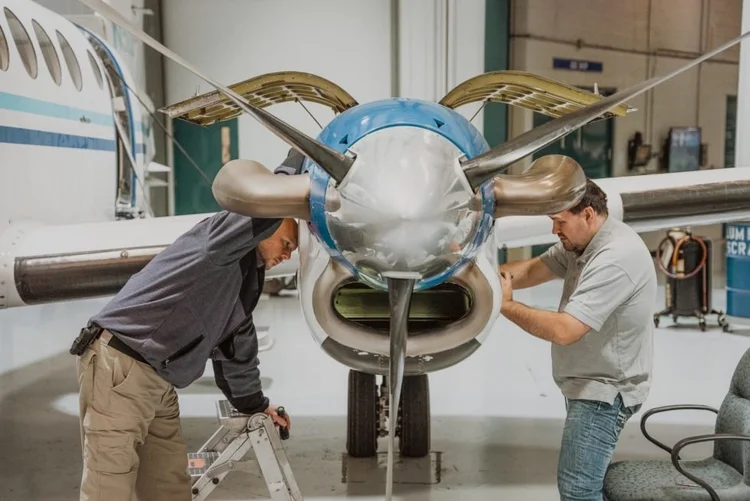 Two Dynamic Aviation coworkers working together on an aircraft engine in a hangar