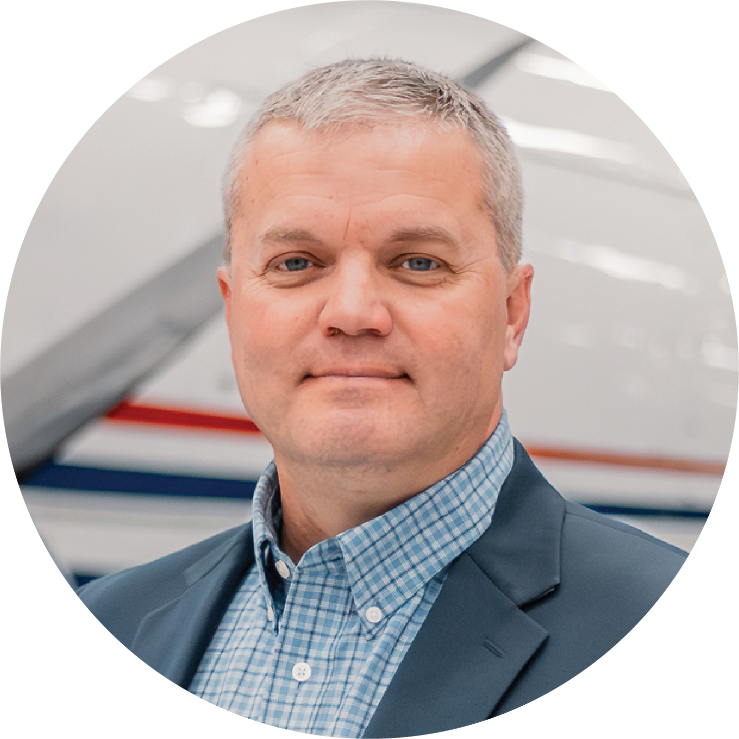A man in a black suit jacket and a checkered shirt standing in front of a backdrop with the logo of the Association of the United States.