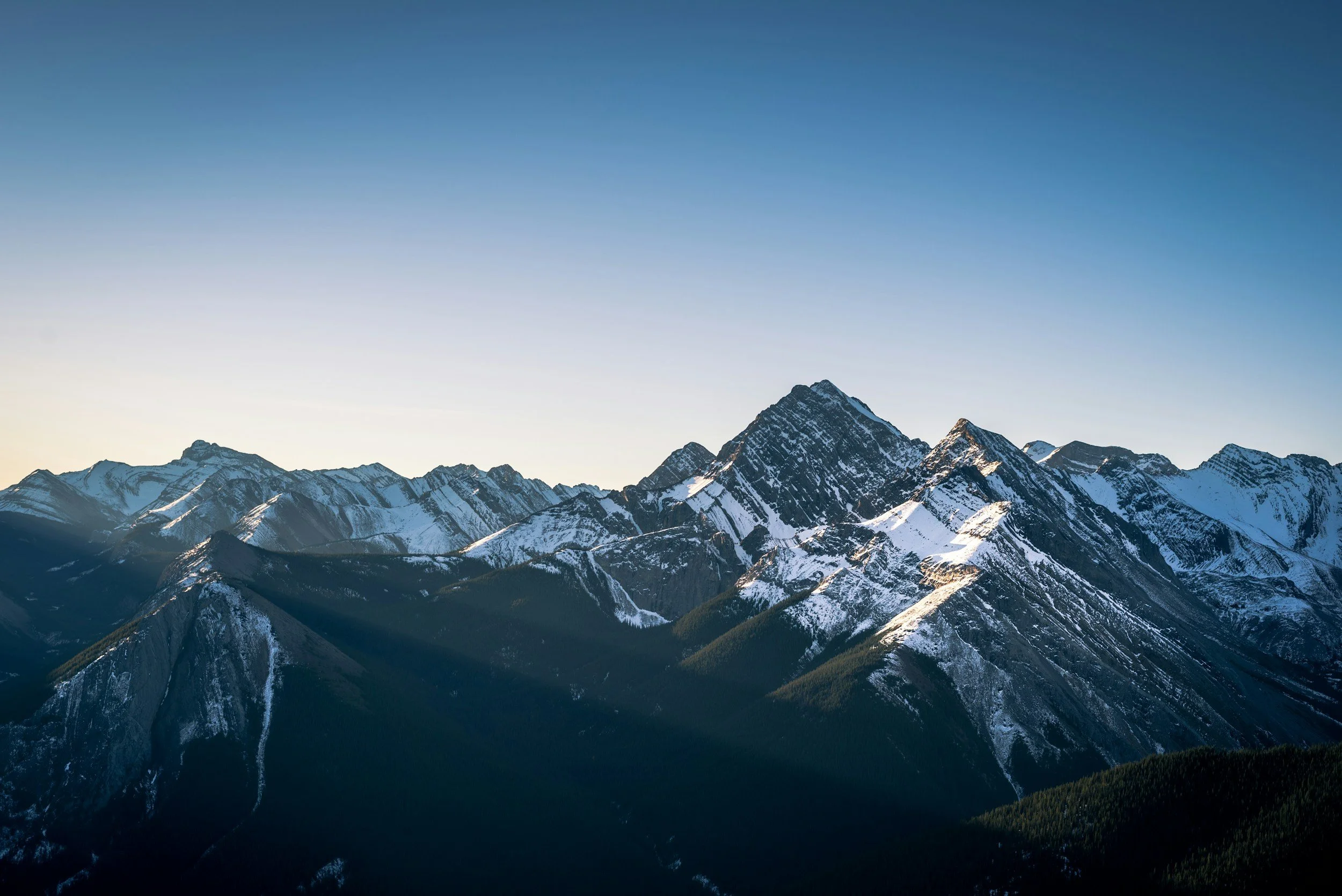 Snow-covered mountain peaks under a clear blue sky at sunrise or sunset.