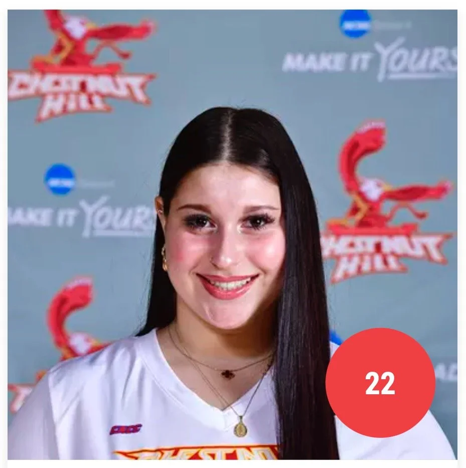 A young woman with long dark hair smiling at the camera. She is wearing a white shirt with a logo and jewelry.