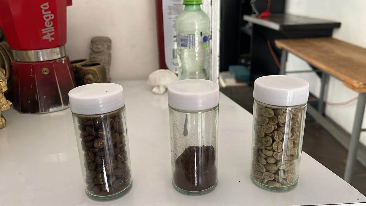Three glass jars with white lids containing roasted coffee beans, ground coffee, and green coffee beans on a white surface.