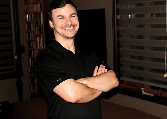 Un homme souriant avec les bras croisés dans une pièce moderne.