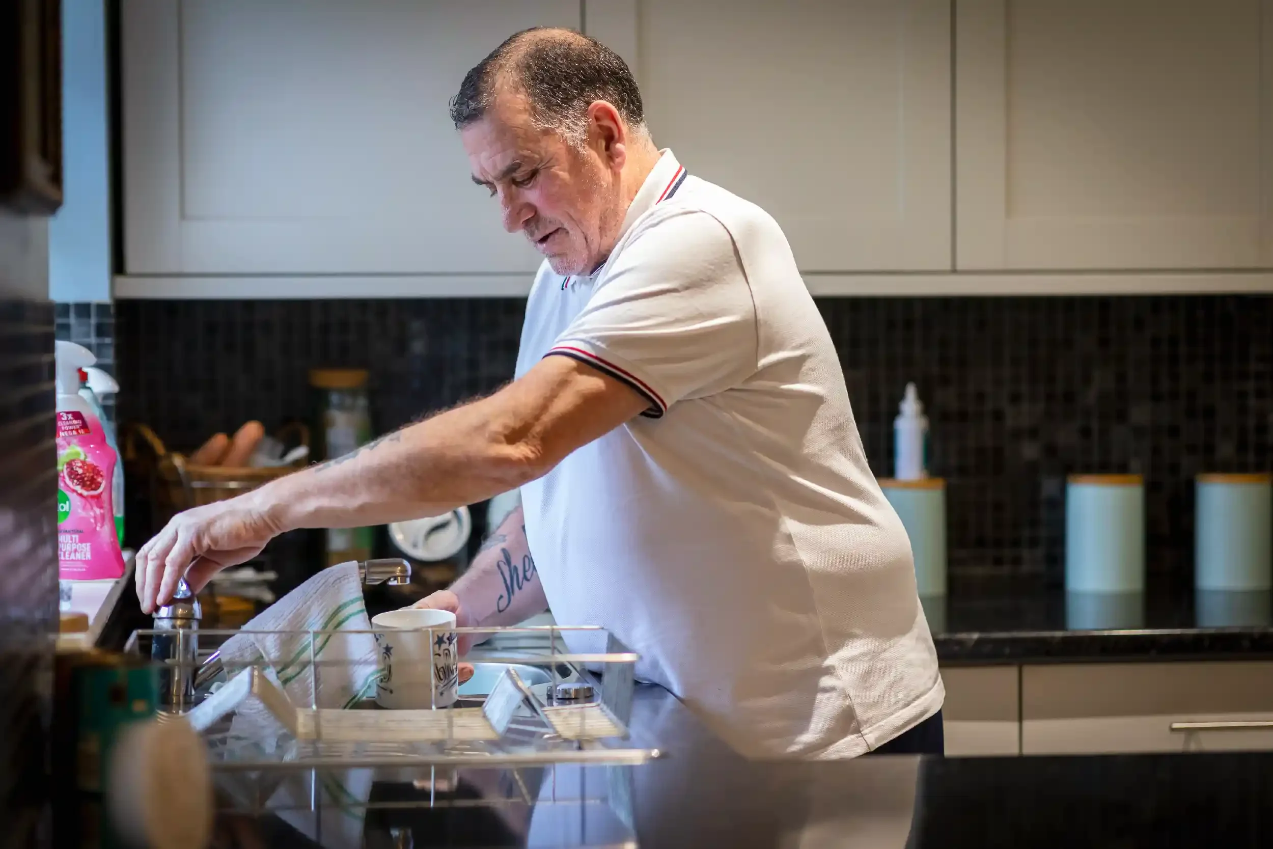 An older man washing dishes in a kitchen.