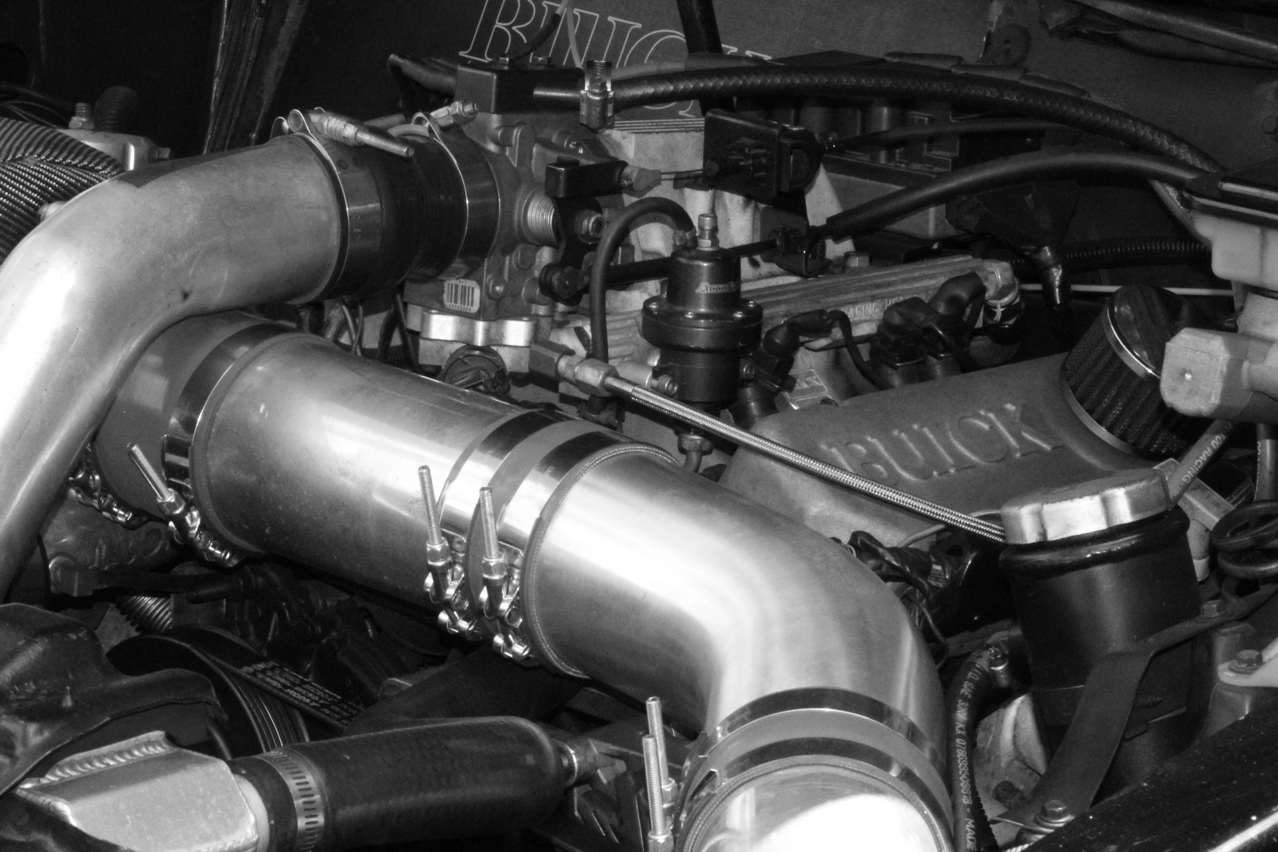 Close-up of a race car engine with various metal components, hoses, and wiring visible.