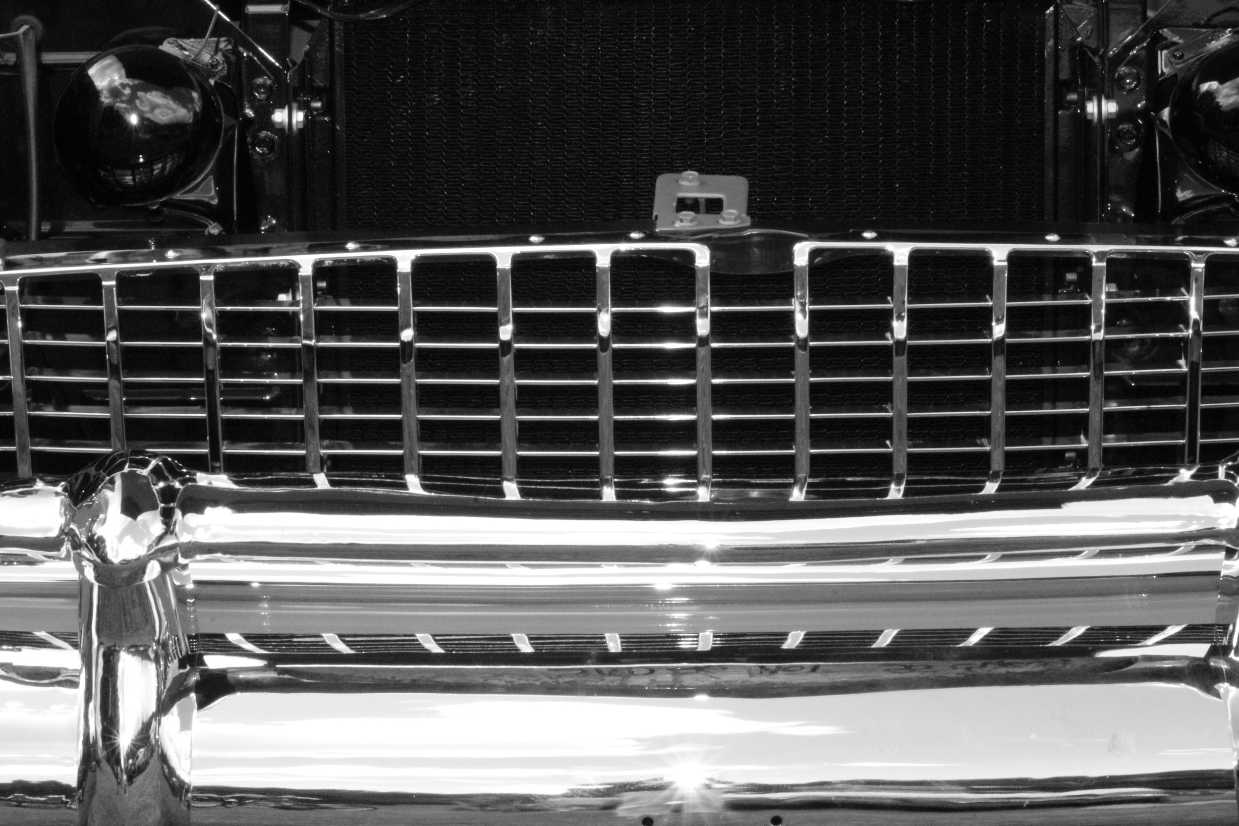 Front view of a classic car grill with chrome details, black radiator, and round headlights on either side.