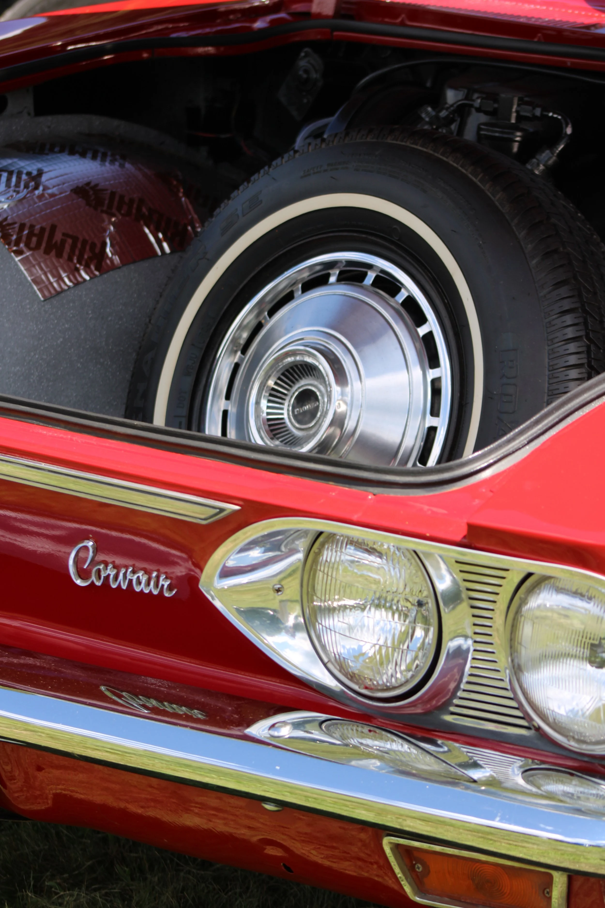 Close-up of the front of a vintage red Chevrolet Corvette, showcasing the headlight, chrome bumper, and part of the windshield.