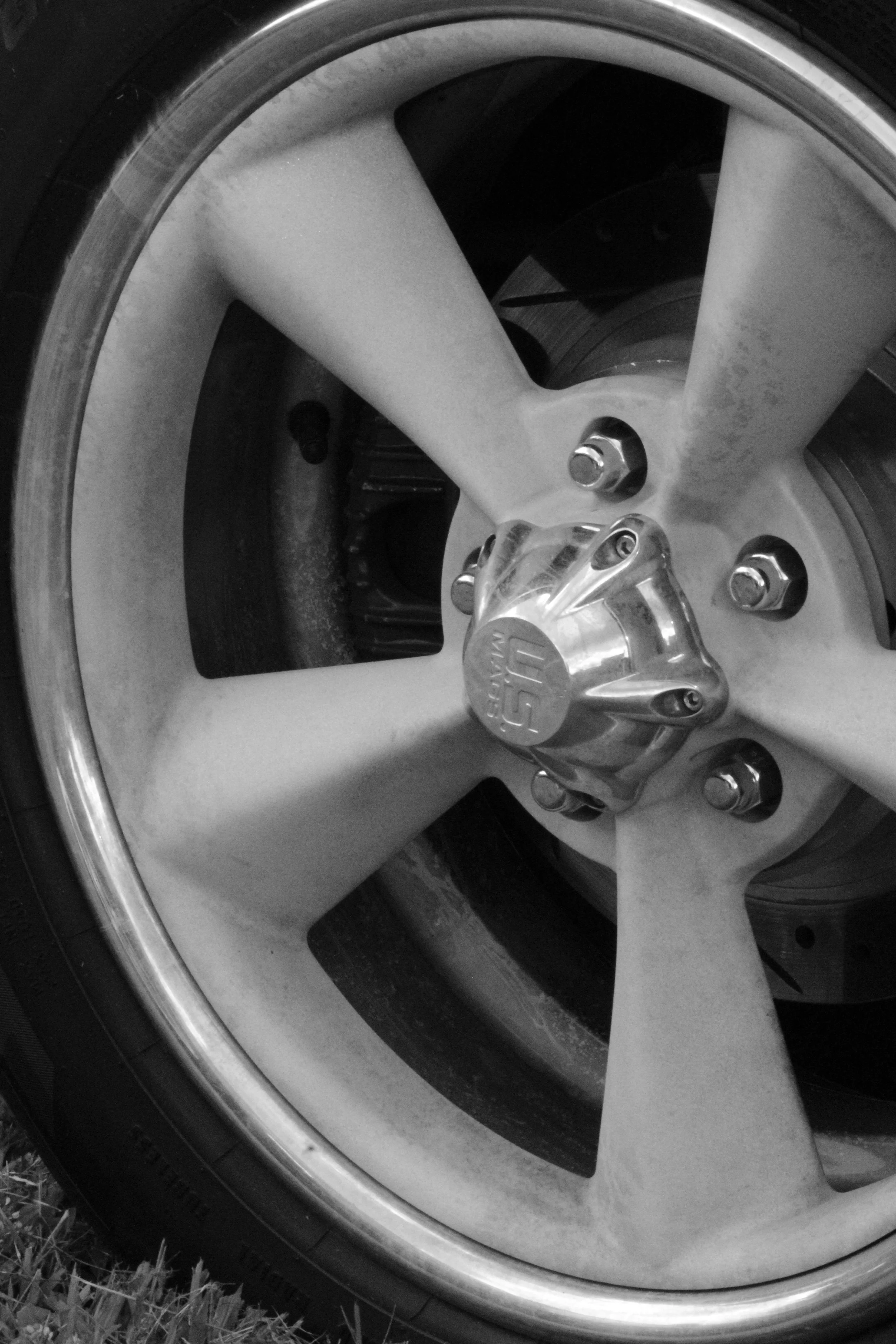 Close-up of a car wheel with a silver alloy rim and black tire, parked on grass.