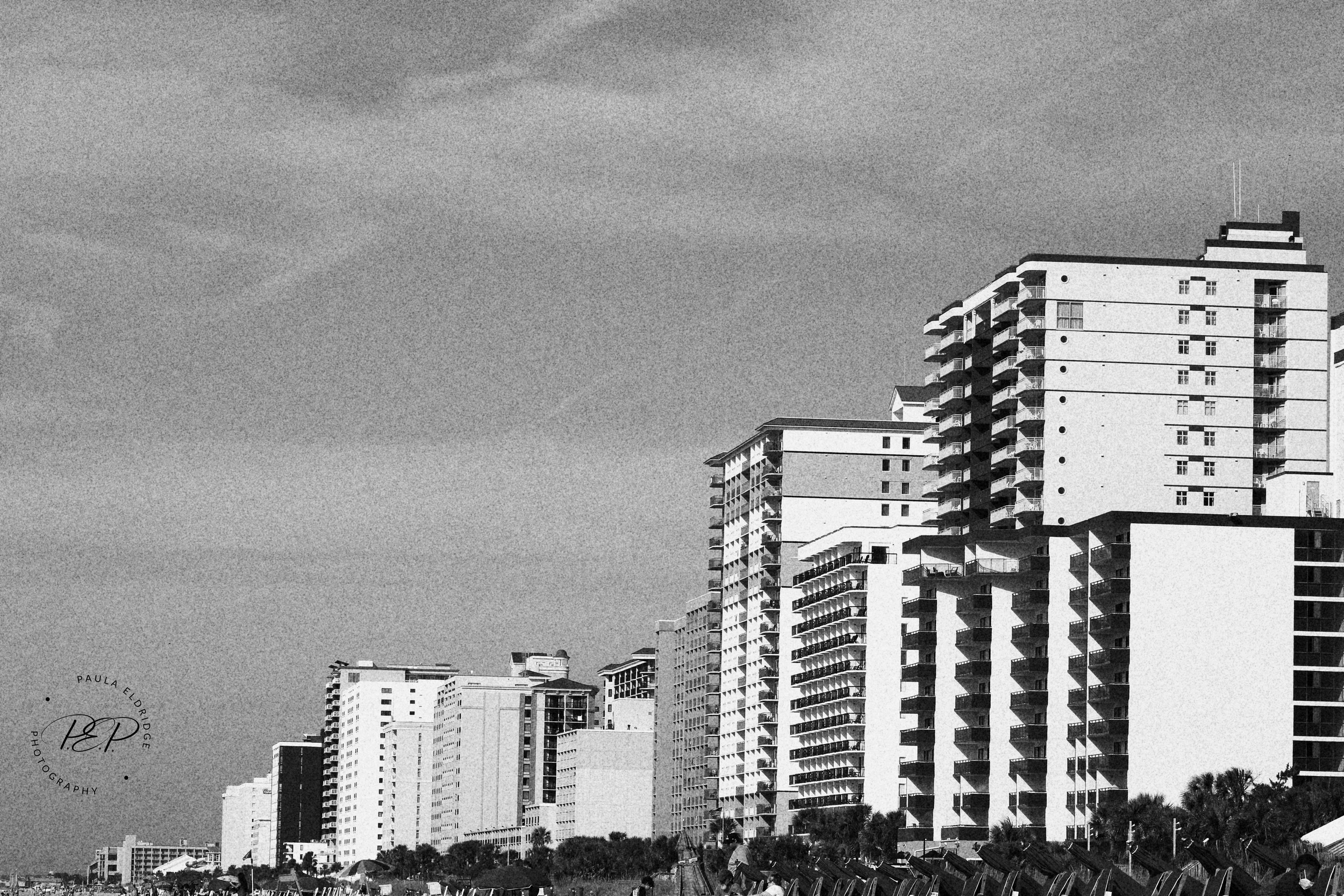 Black and white photo of a skyline with tall modern buildings, some with balconies, under a cloudy sky.