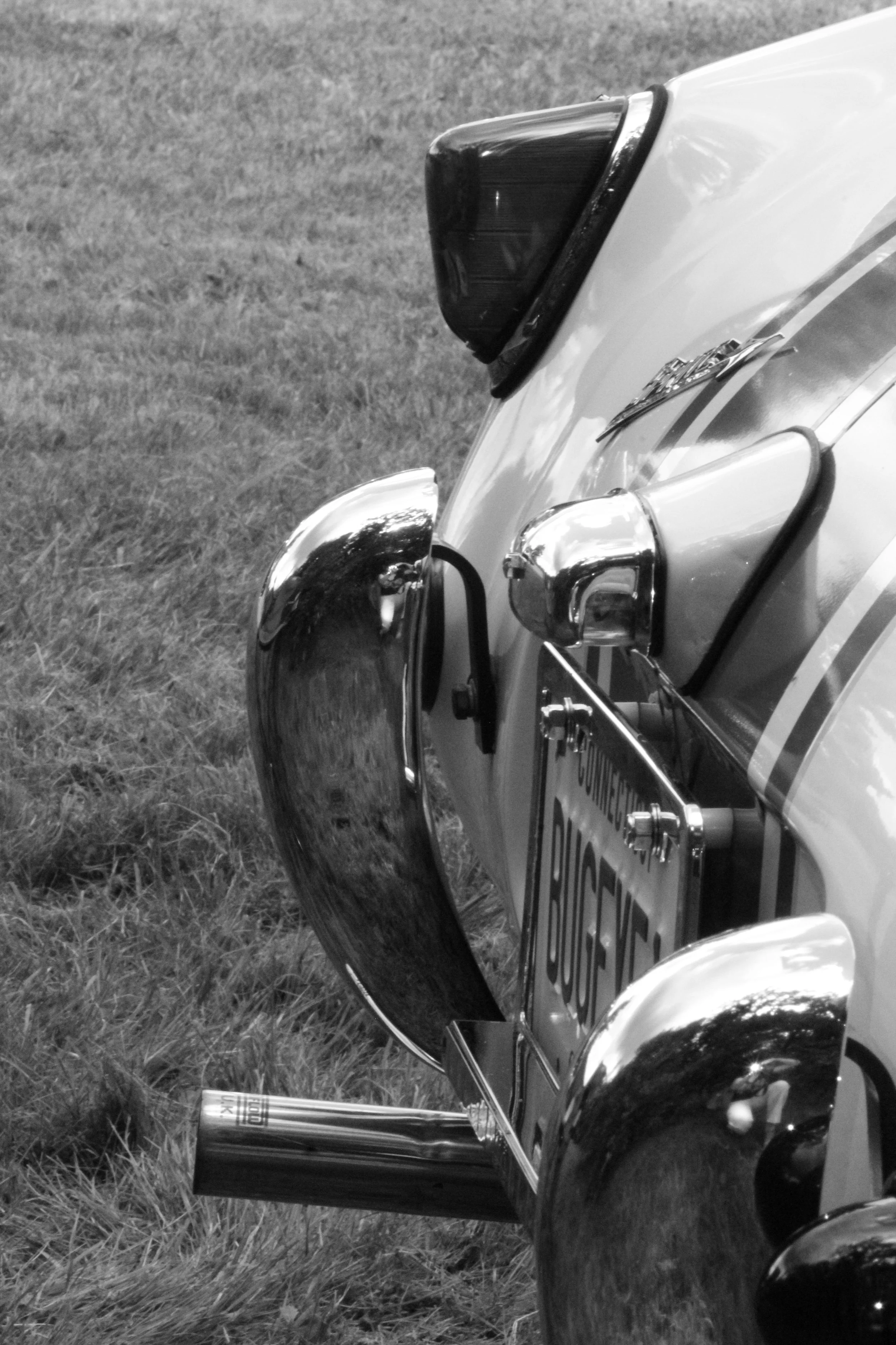 Close-up of a police car's front, showing the headlight, bumper, and part of the grille, with a grassy area in the background.