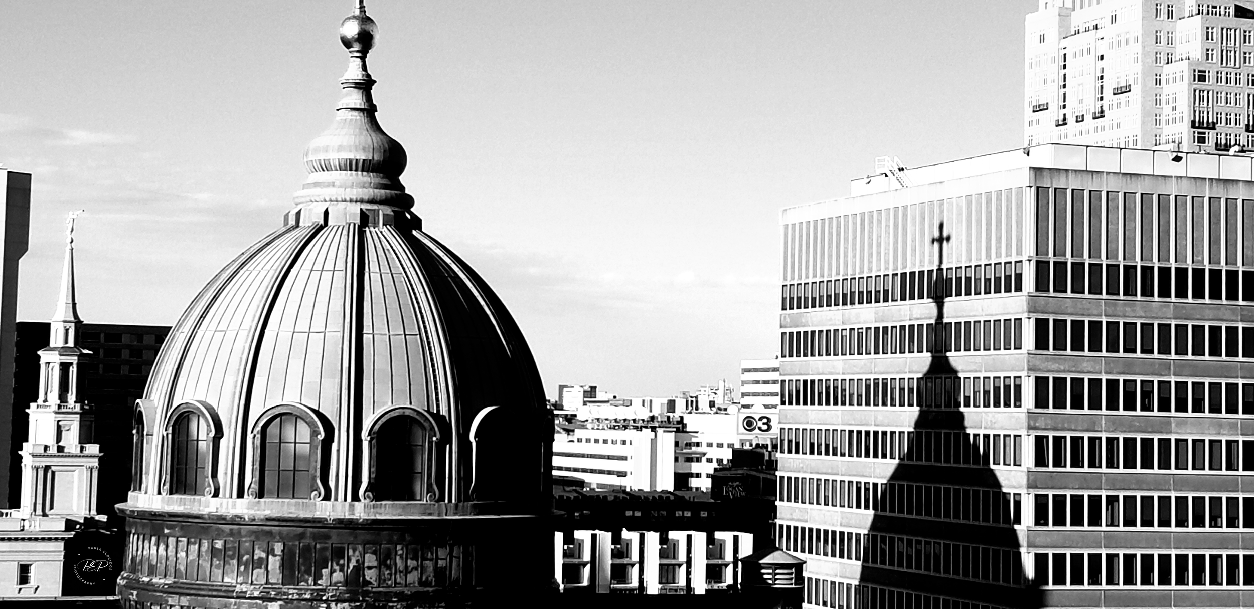 Black and white photo of city skyscrapers with prominent dome structure and shadow of a cross on a building.