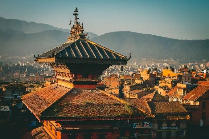 Traditional Nepalese temple with intricate roof details in an urban area with mountains in the background.