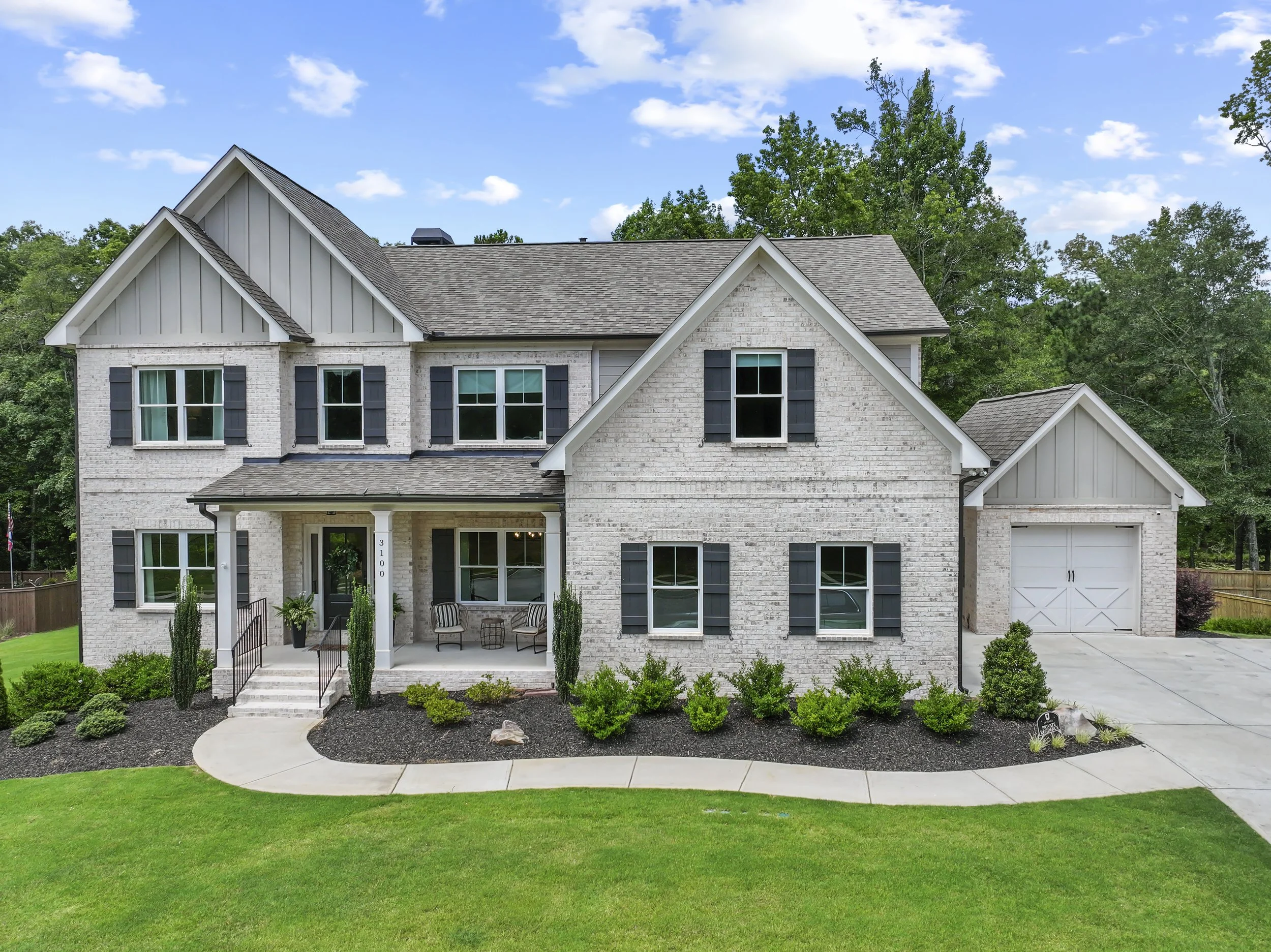 Front view of a two-story house with a brick facade, black shutters, and a gray roof, surrounded by a well-maintained lawn and landscaping.