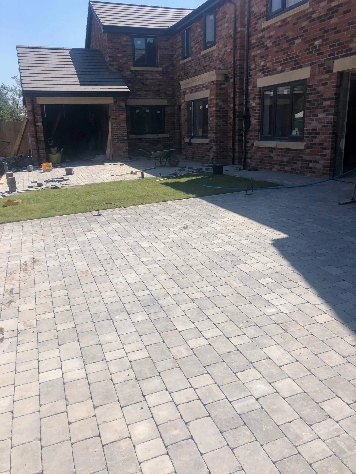 Residential backyard with a house under construction, featuring paving stones, a small grassy patch, and construction tools.