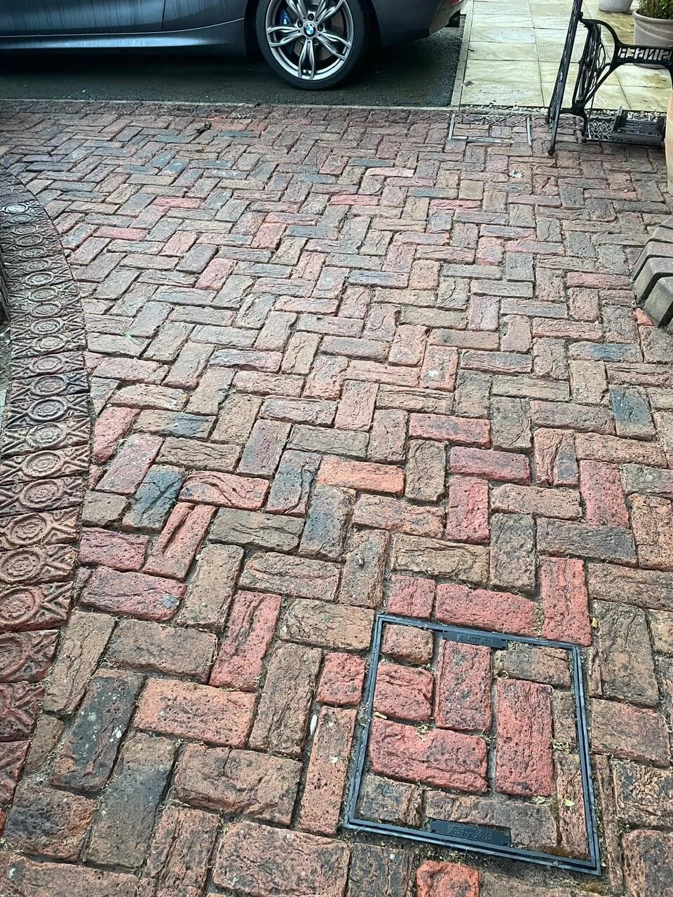 Brick driveway with a metal hatch door and a parked car in the background.