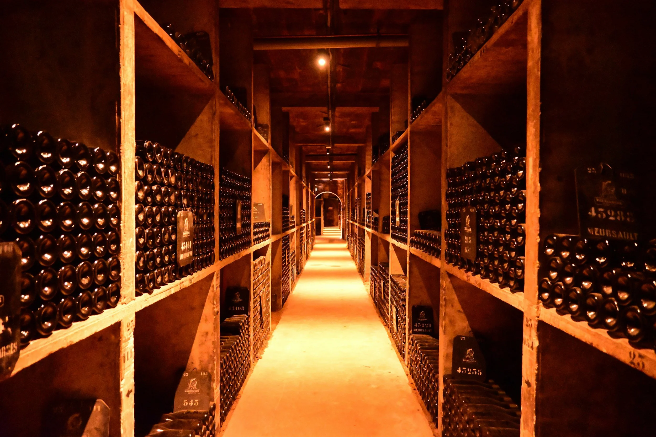 A wine cellar with rows of shelves filled with wine bottles, illuminated by warm lighting.