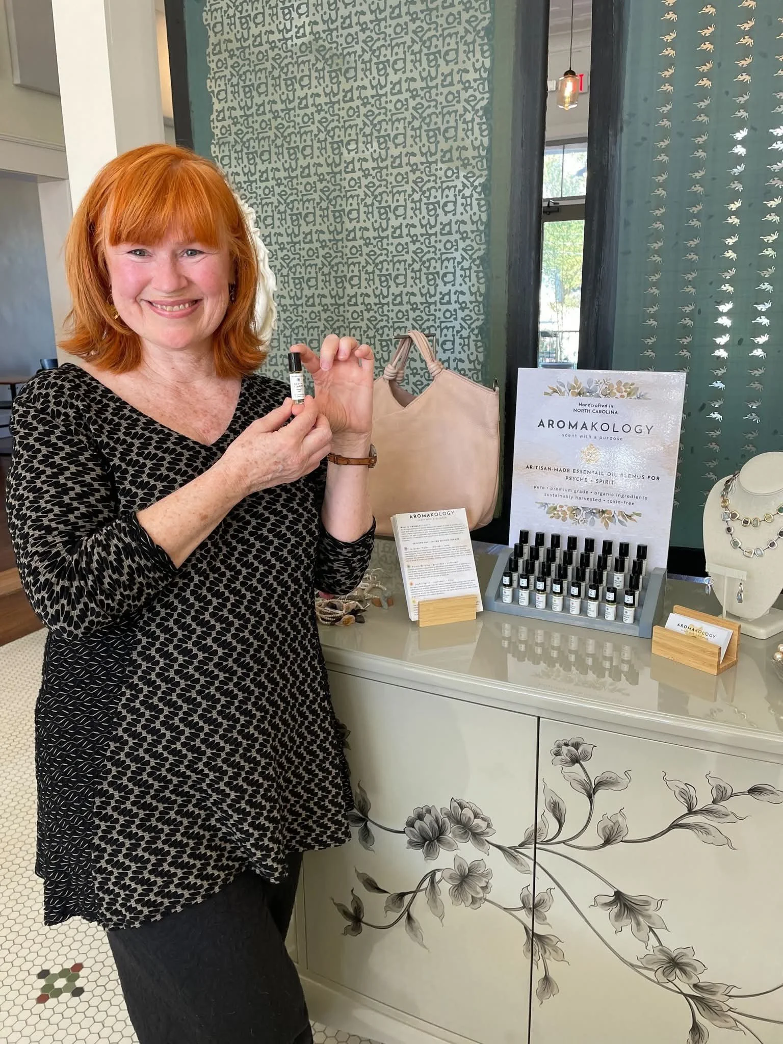 Kira, founder of Aromakology Scent Studio, holding a botanical oil bottle standing in front of her botanical essences products.