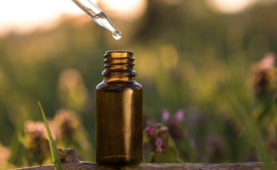 Dropper dripping liquid into an amber glass bottle outdoors at sunset.