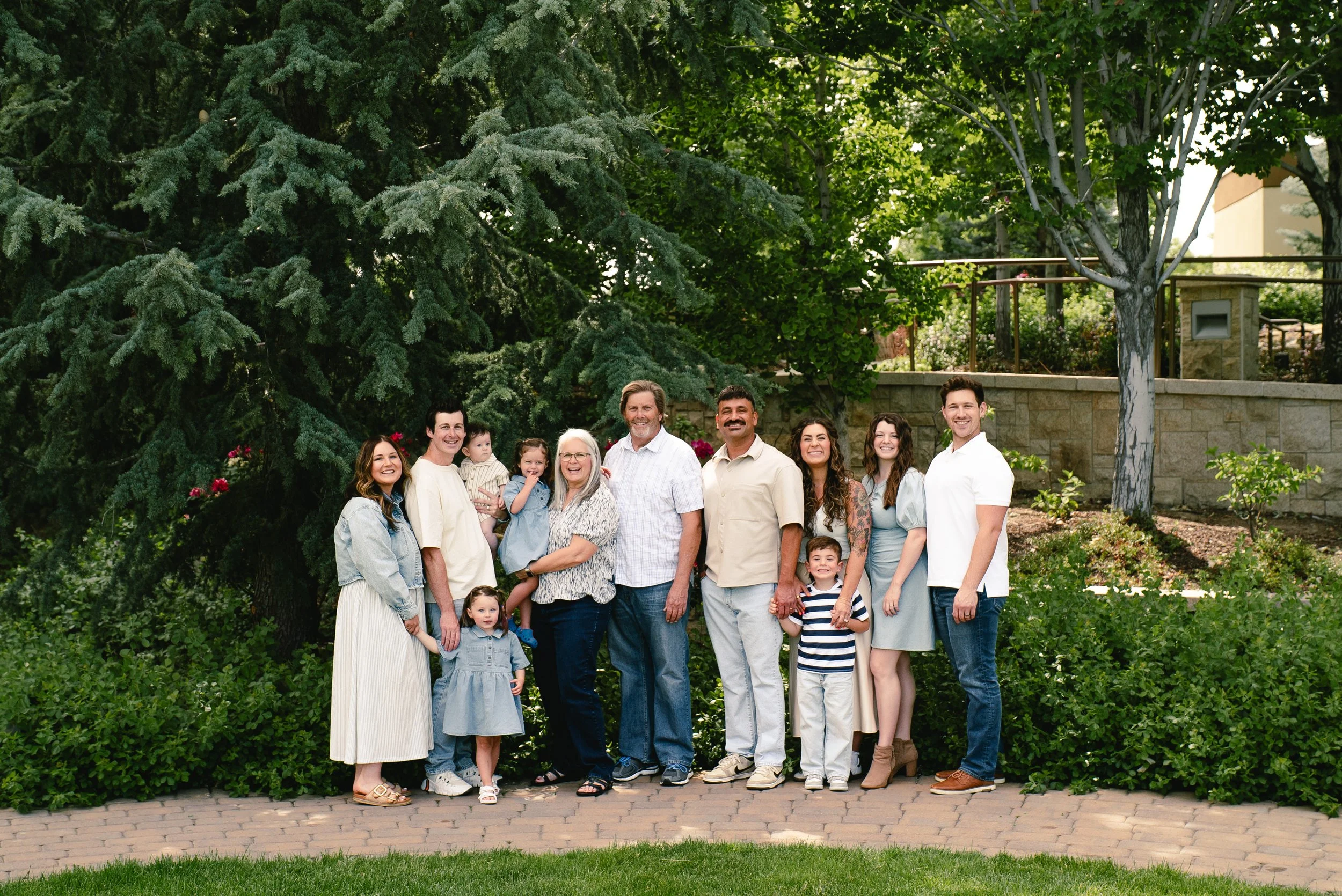 Family group standing outdoors in front of trees, smiling for the camera at a park or garden.