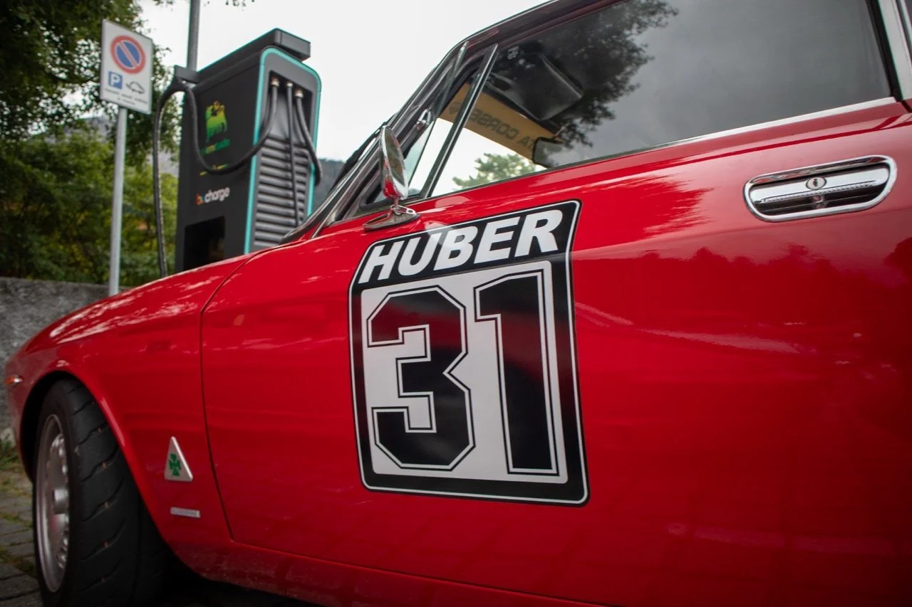 Auto da corsa rossa con il numero 31 e la scritta Huber, collegata a una stazione di ricarica per veicoli elettrici in background.