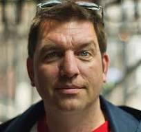 Portrait of a man with brown hair and a serious expression, wearing a dark jacket.