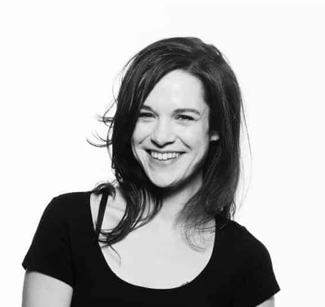 Black and white photo of a woman with dark hair smiling, wearing a black top.