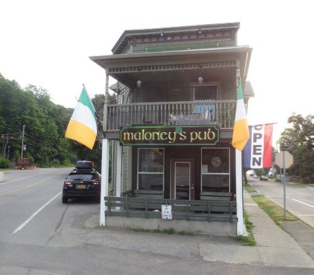 Exterior of Maloney's Pub, a two-story building with a balcony, flags, and an 'OPEN' flag outside.  Maloney's Pub is only a few minutes away by foot from The Irish Cardinal.