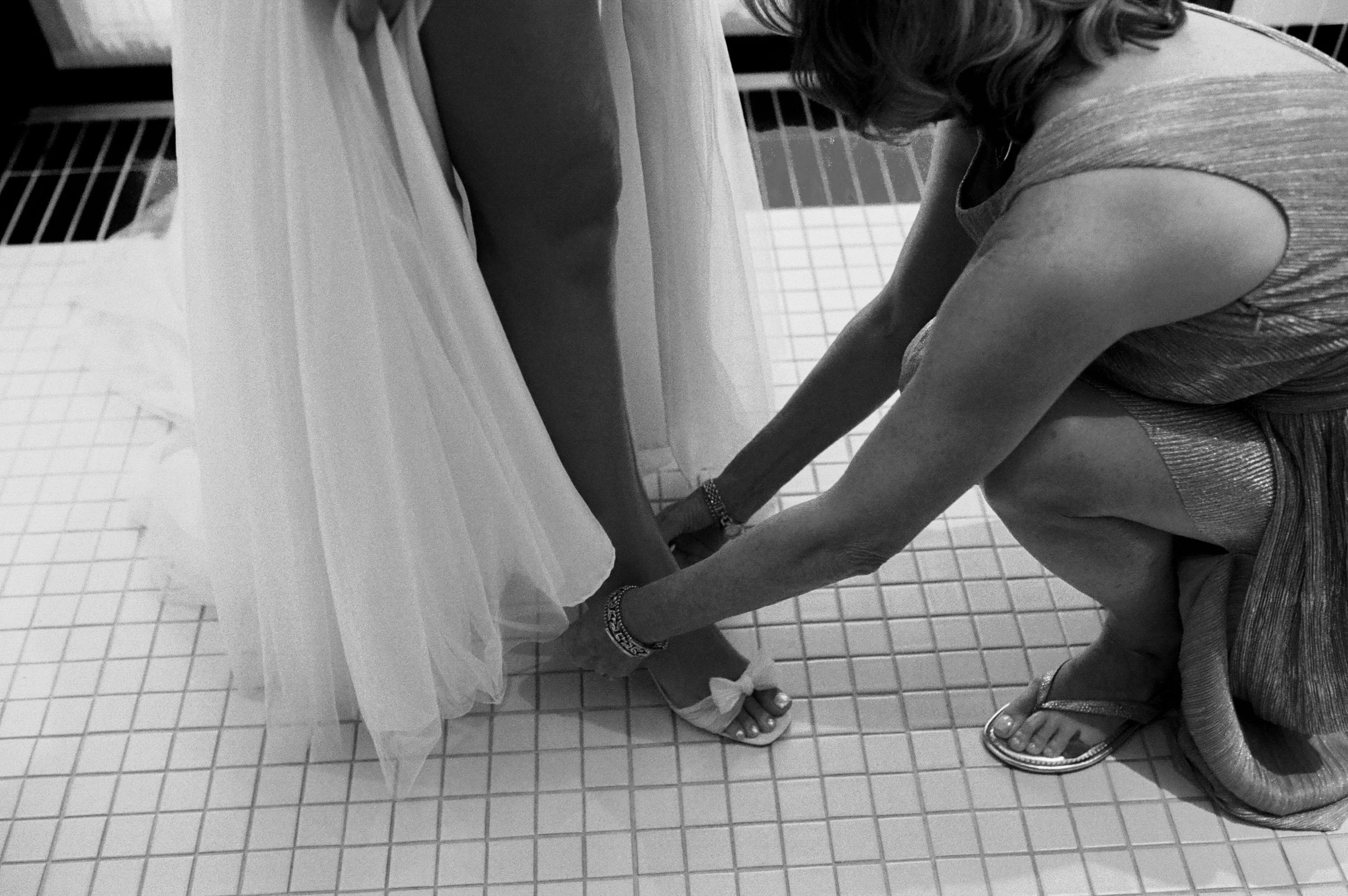 Black and white photo of a bridesmaid helping fasten the bride’s wedding heels before the ceremony at Shinola Hotel