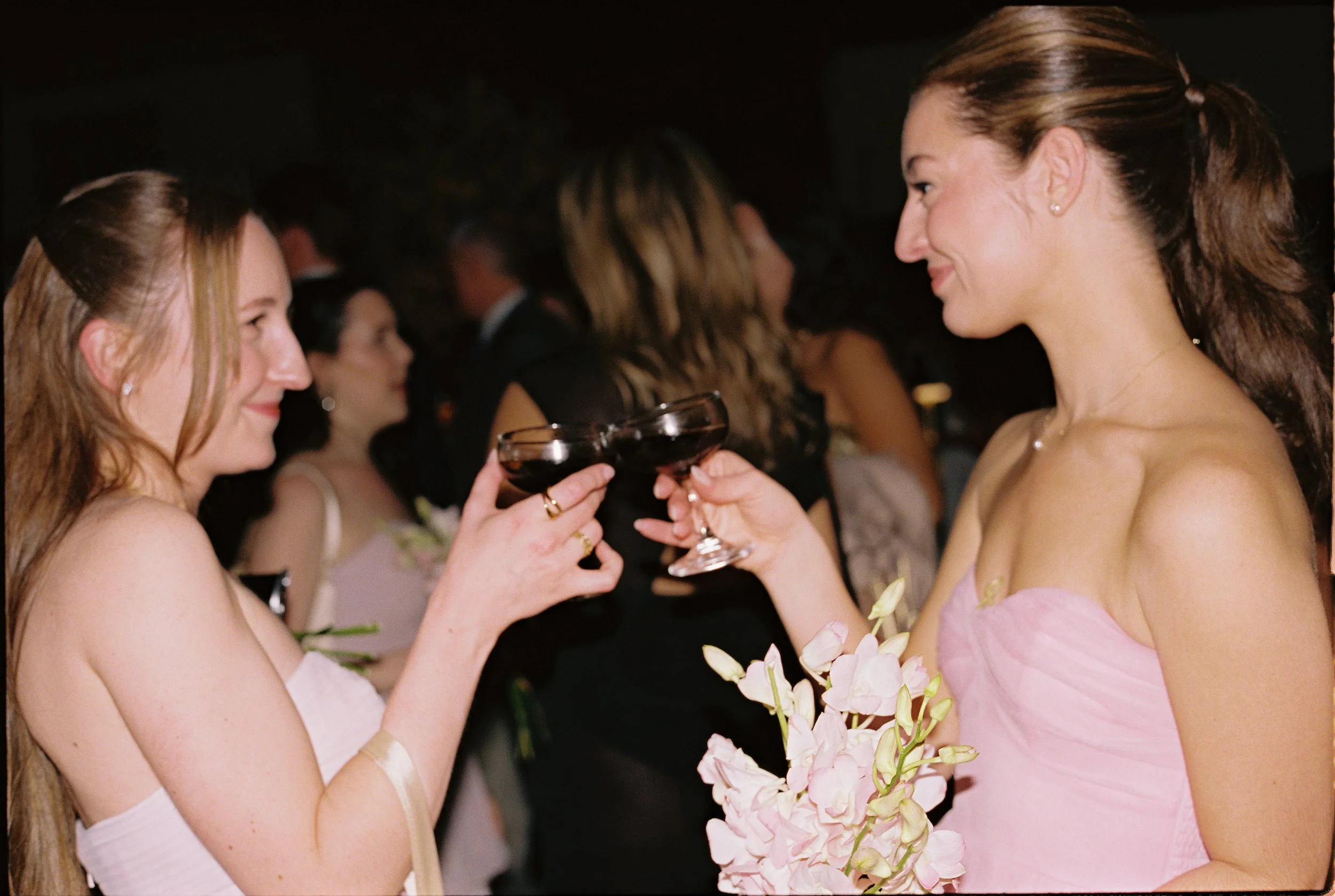 Bridesmaids in blush pink dresses clinking coupe glasses together during the wedding reception celebration.