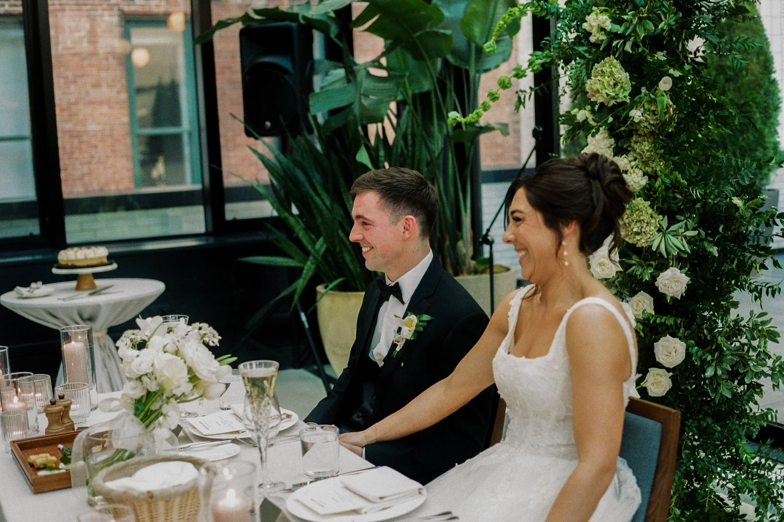 Bride and groom smiling during speeches at their intimate wedding reception surrounded by florals and candlelight