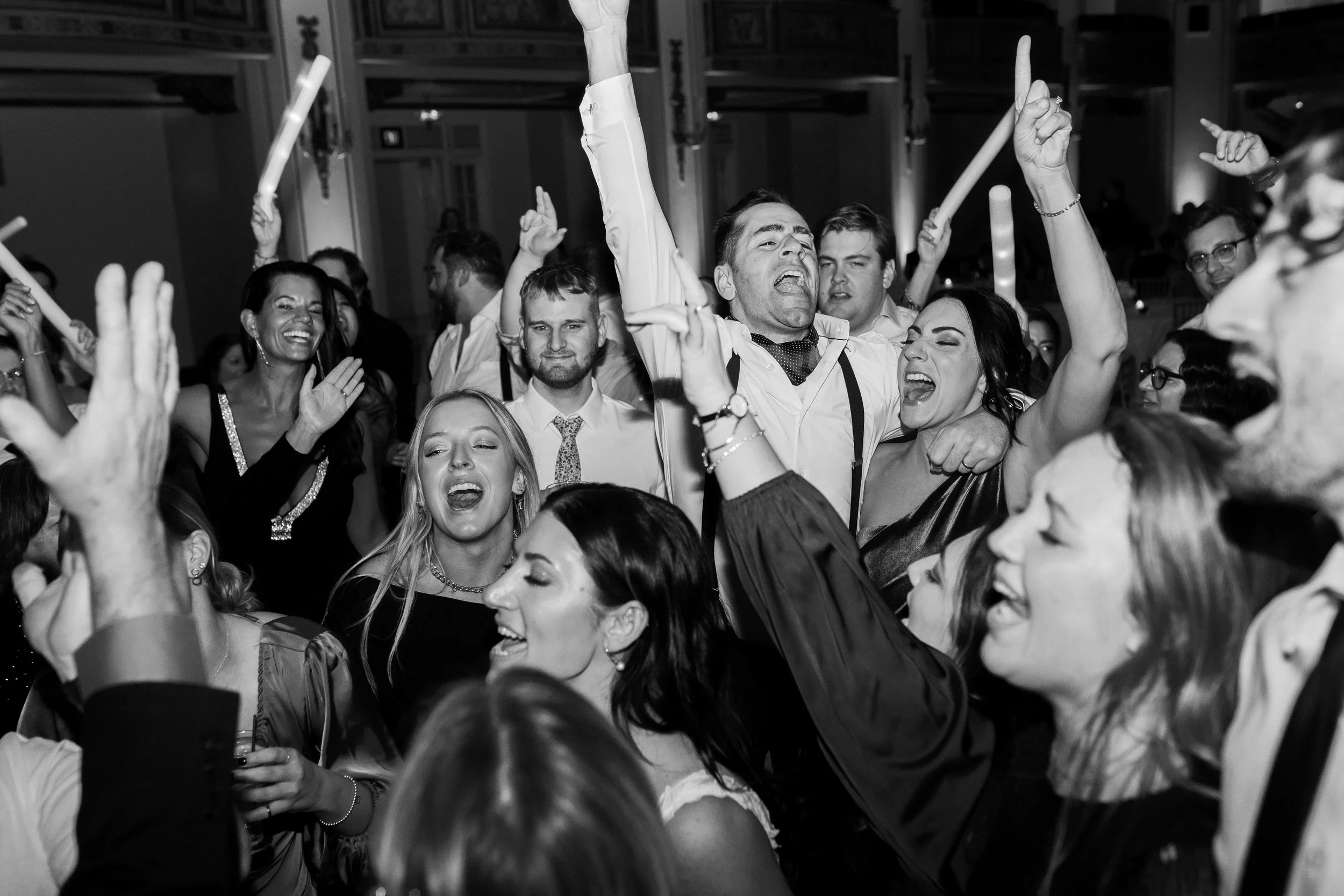 A black and white photo of the bride and wedding guests dancing and singing on the dance floor