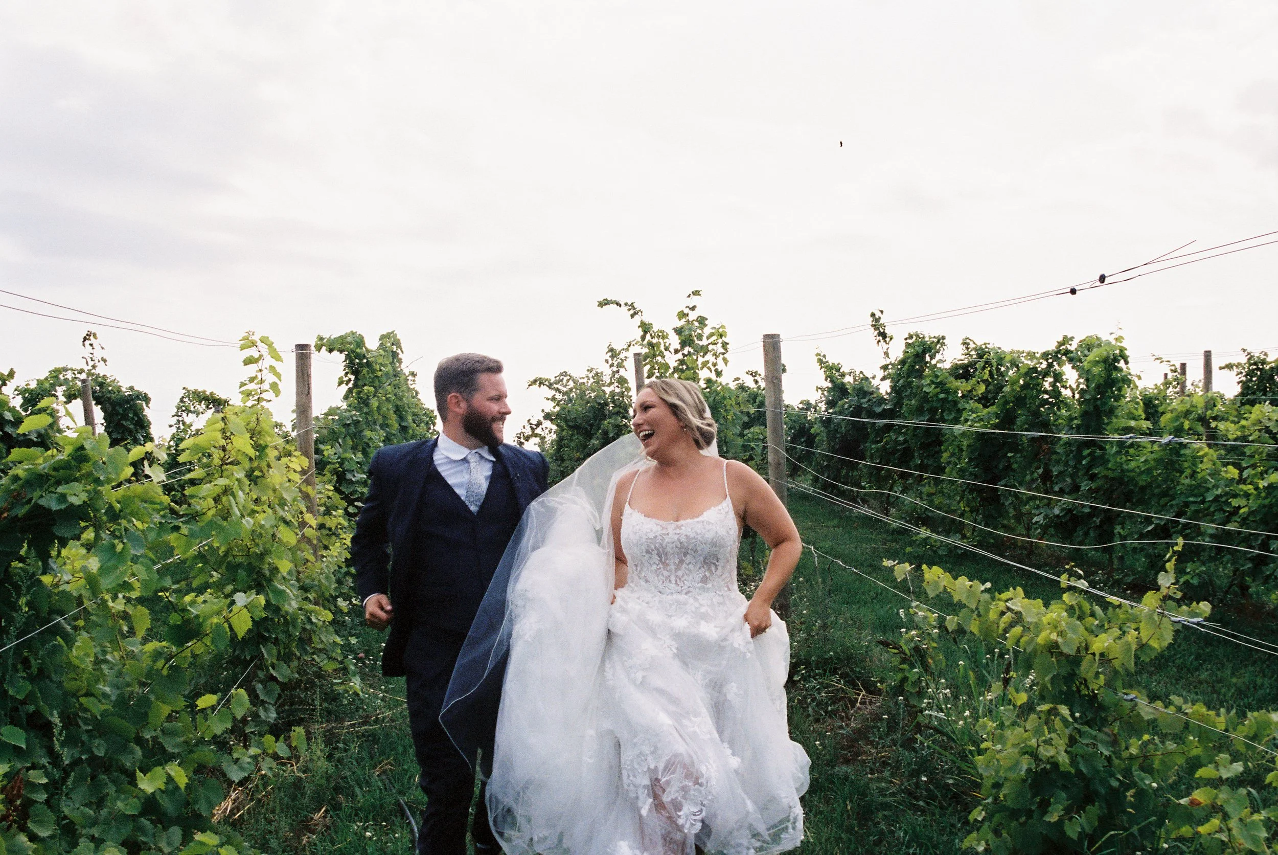 Bride and groom laughing together while walking through vineyard rows during their Northern Michigan vineyard wedding portraits.