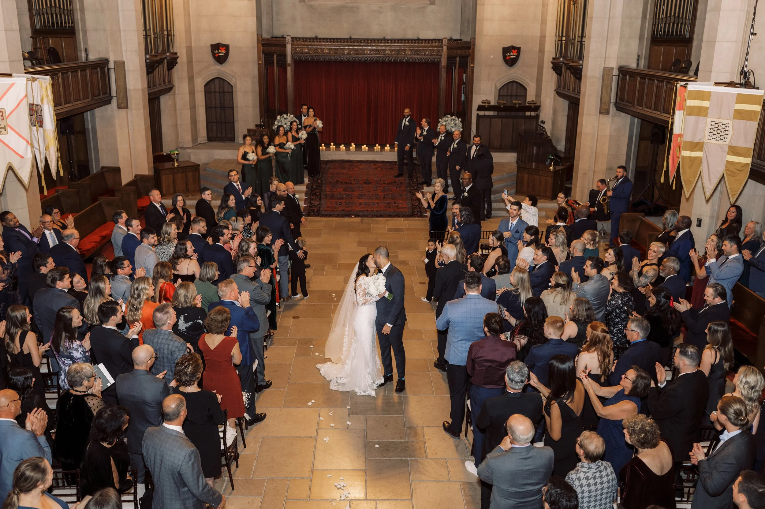 Bride and groom sharing a kiss in the aisle as their wedding guests applaud around them.