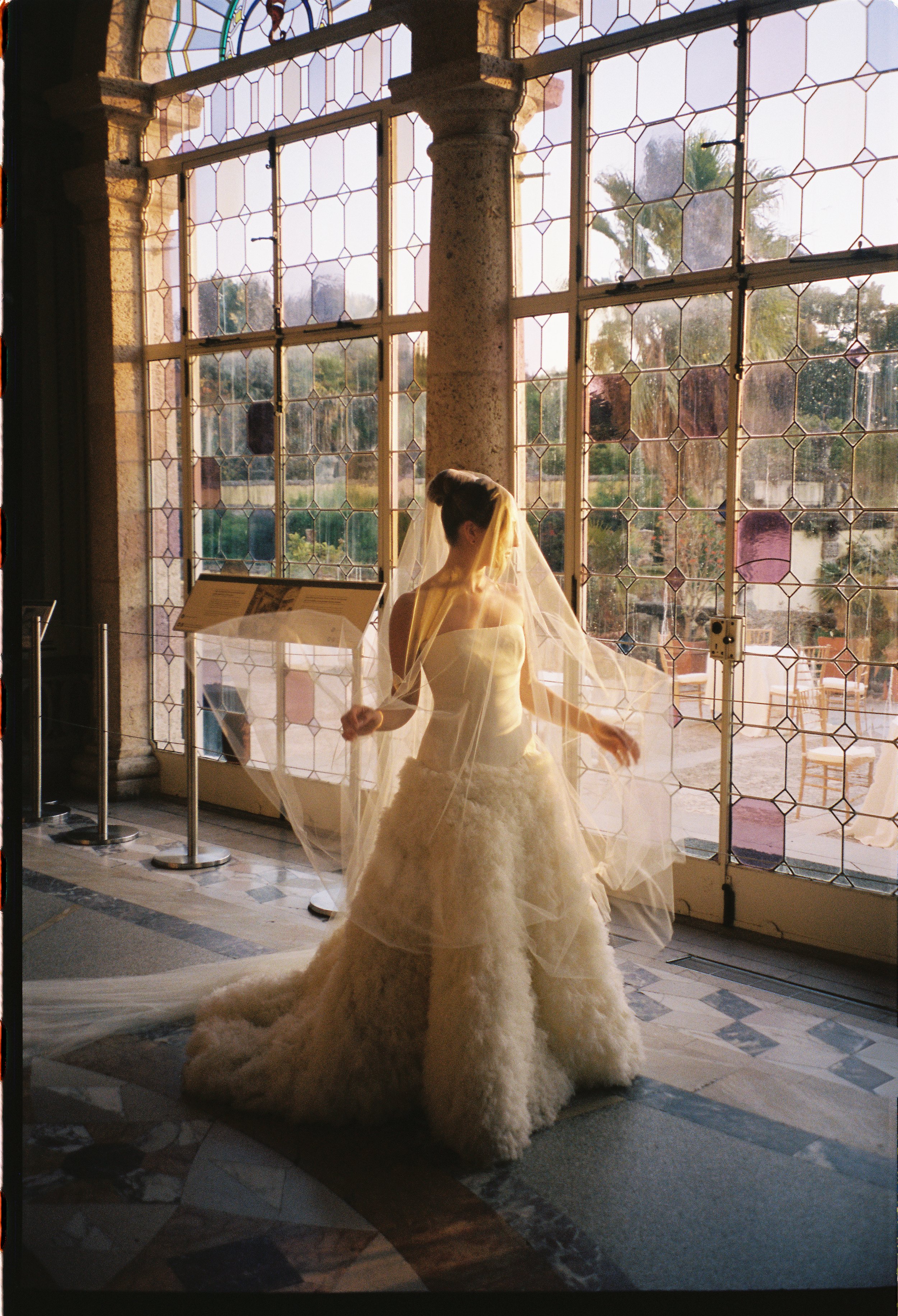 Bride twirling in her wedding gown and veil in front of large stained-glass windows inside Vizcaya Museum and Gardens. (Copy)