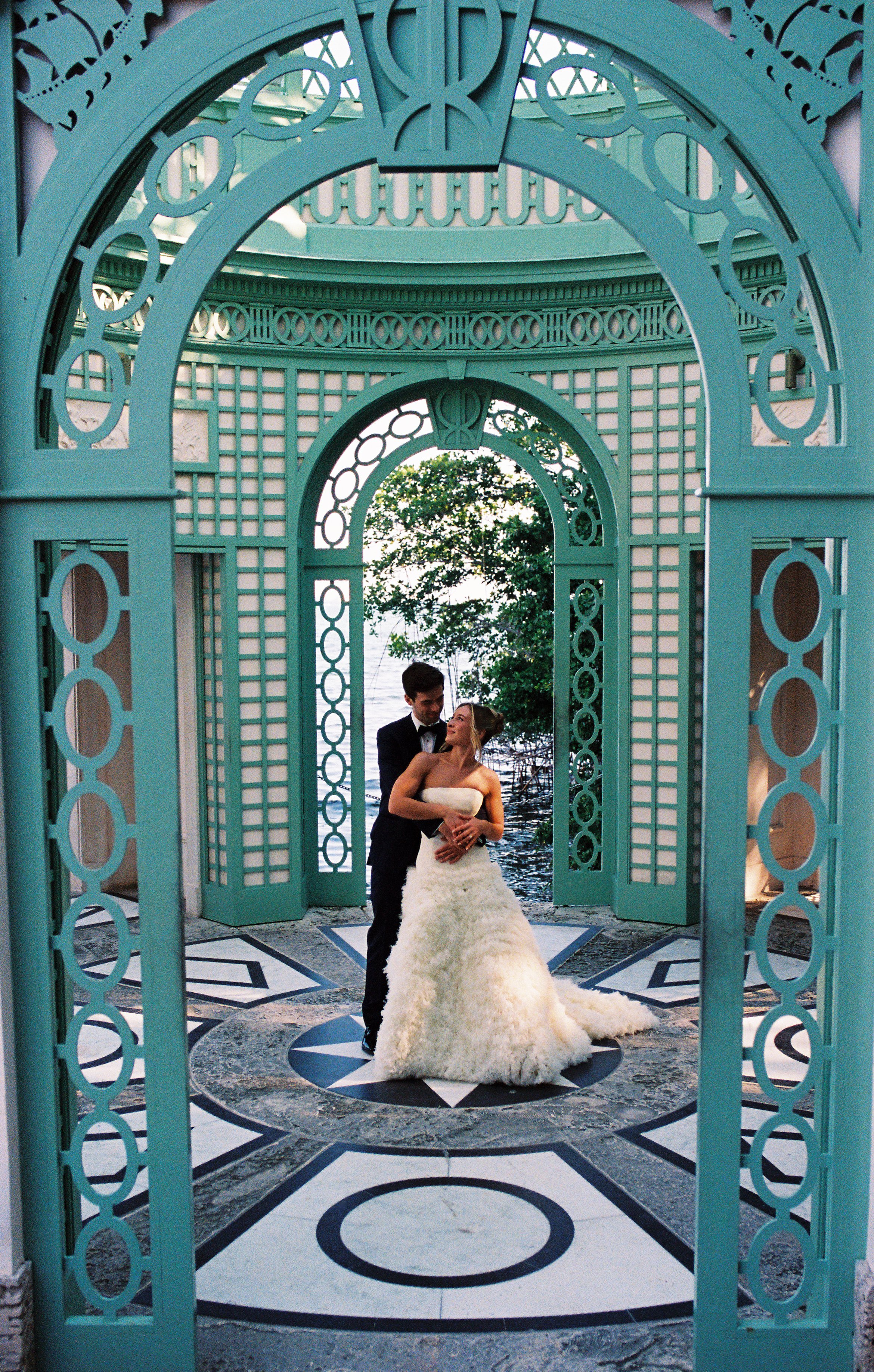 Newlywed couple embracing beneath the teal pavilion overlooking Biscayne Bay at Vizcaya Museum and Gardens. (Copy)