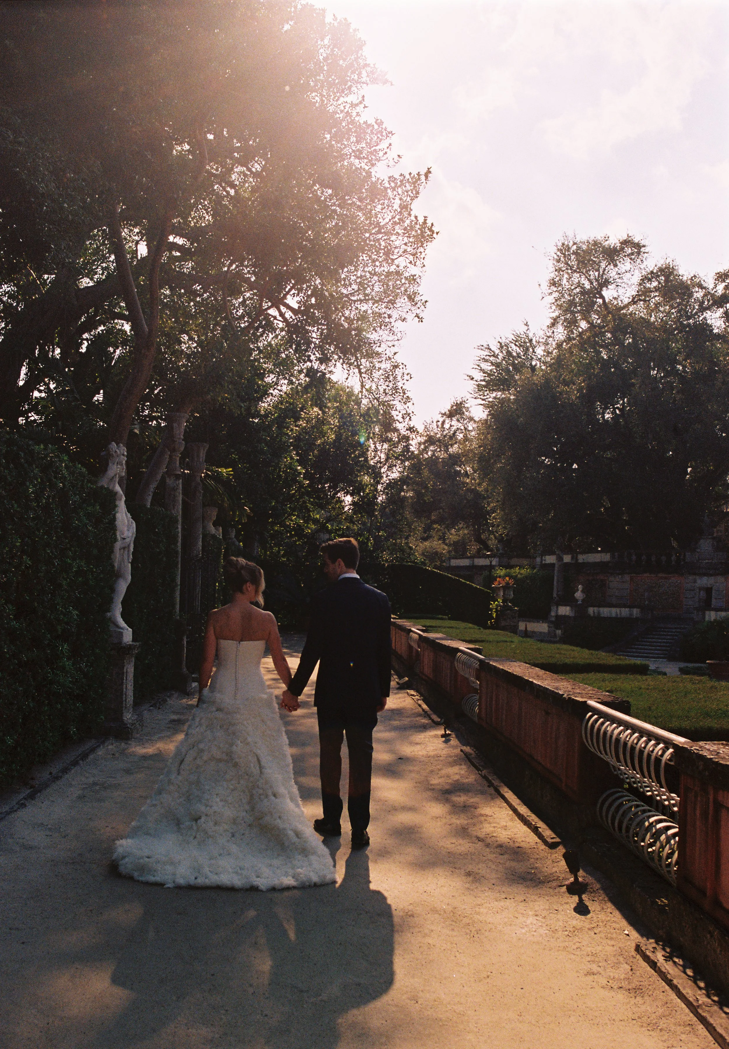 Newly married couple walking hand in hand through the lush gardens at Vizcaya Museum and Gardens during golden hour. (Copy)