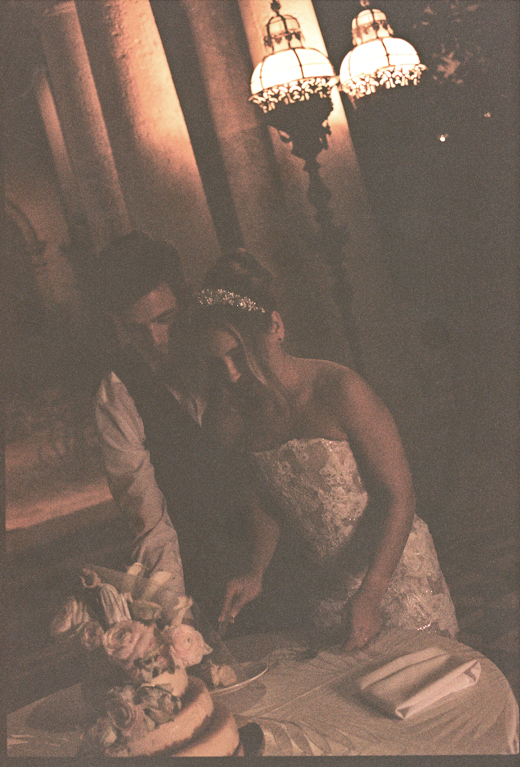 Bride and groom cutting their wedding cake together under warm glowing chandeliers during their Vizcaya Museum and Gardens wedding reception. (Copy)