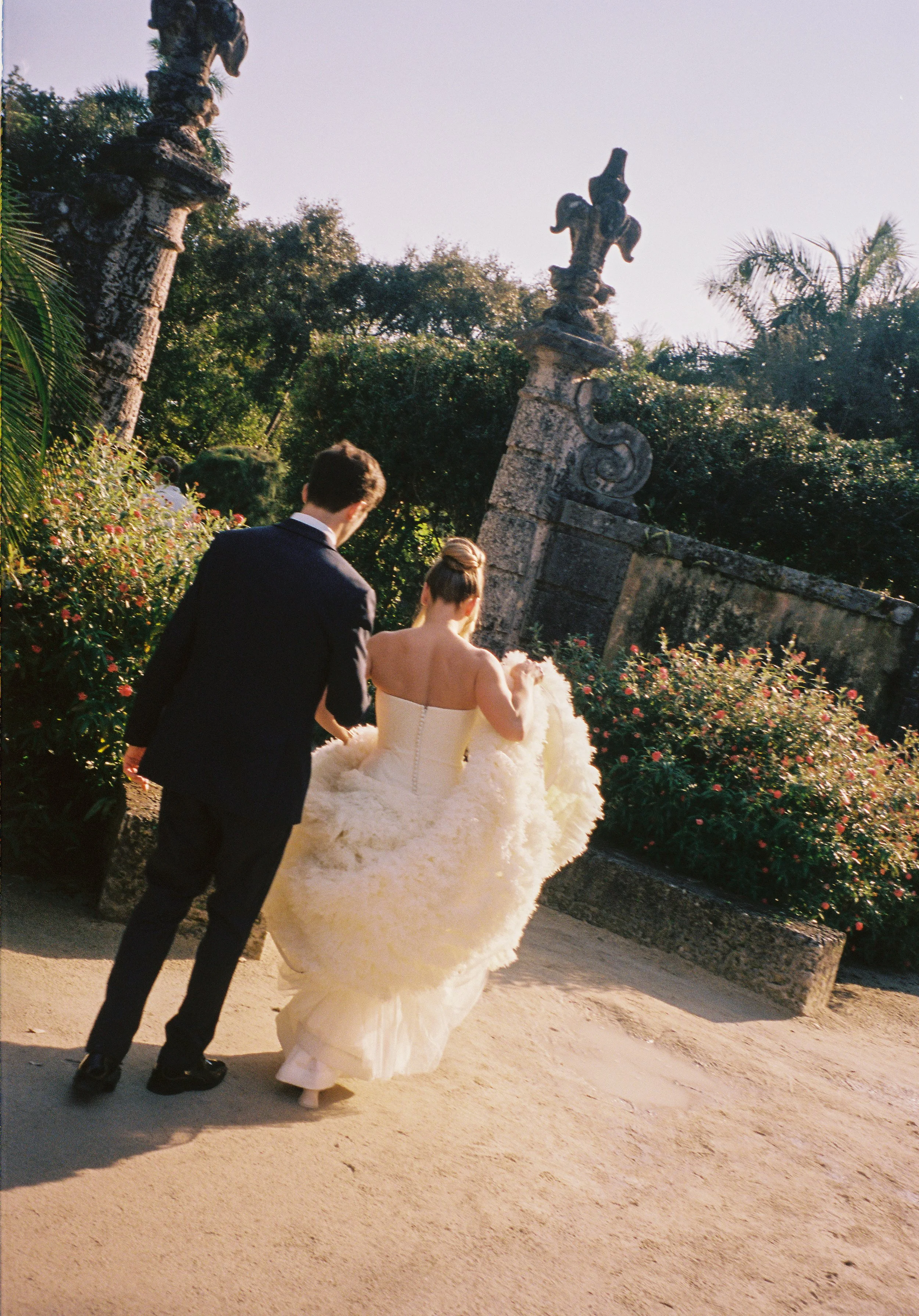 Bride and groom walking through the historic gardens during their Vizcaya Museum and Gardens wedding, surrounded by stone sculptures and lush greenery. (Copy)