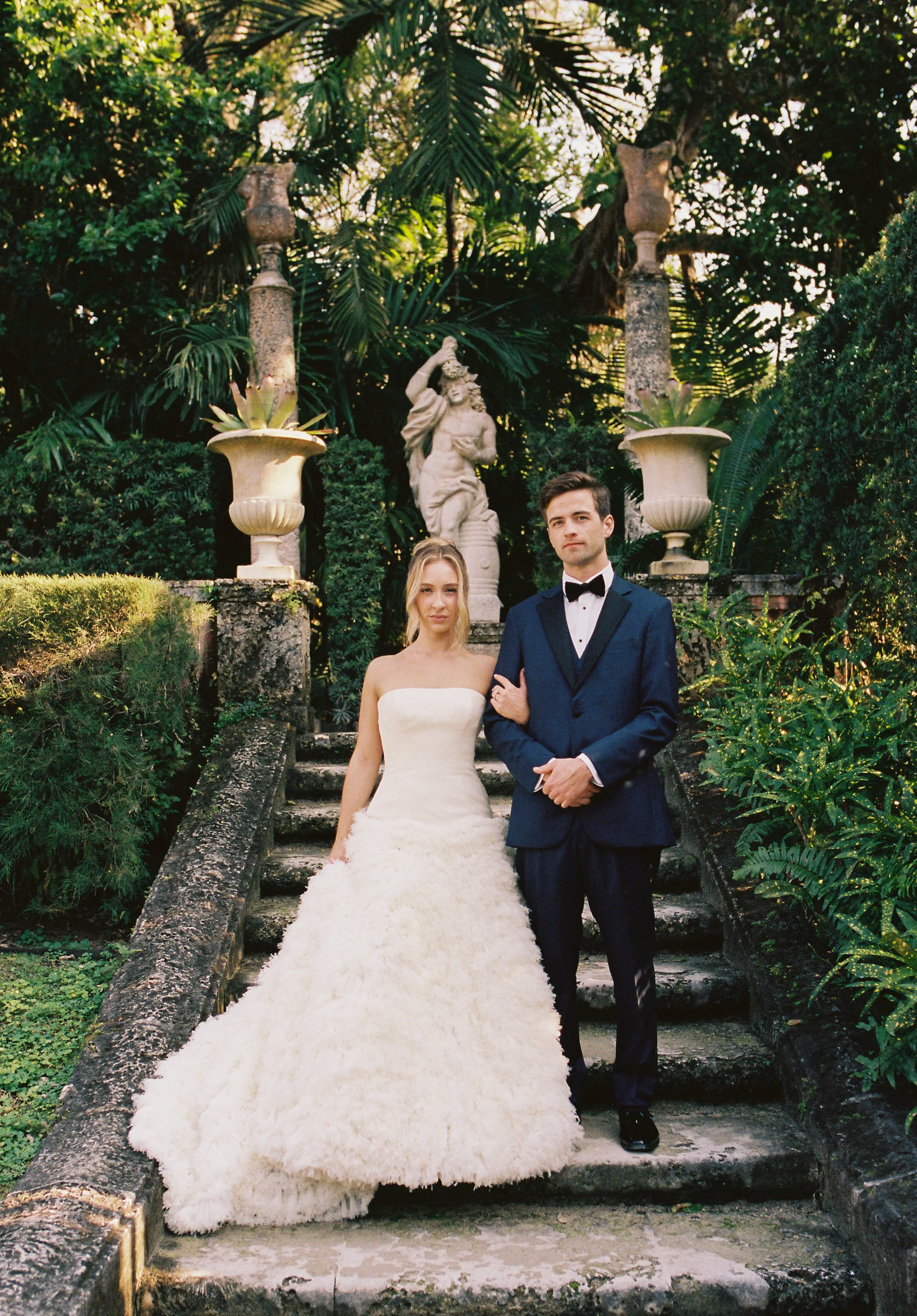 Bride and groom posing together on the garden staircase surrounded by tropical greenery at their Vizcaya Museum and Gardens wedding. (Copy)