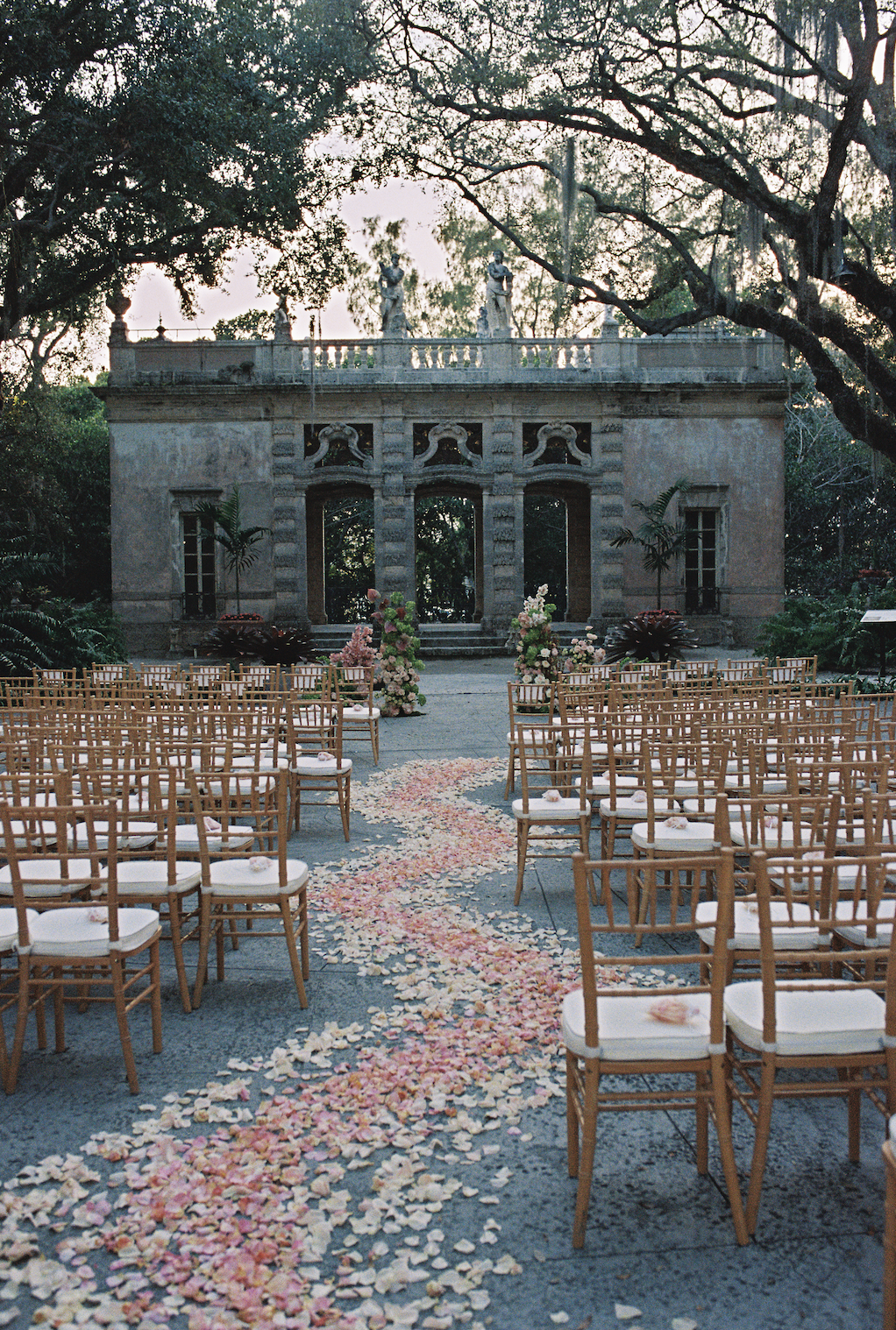 A flower lined aisle showcasing pink petals and ceremony chairs. (Copy)