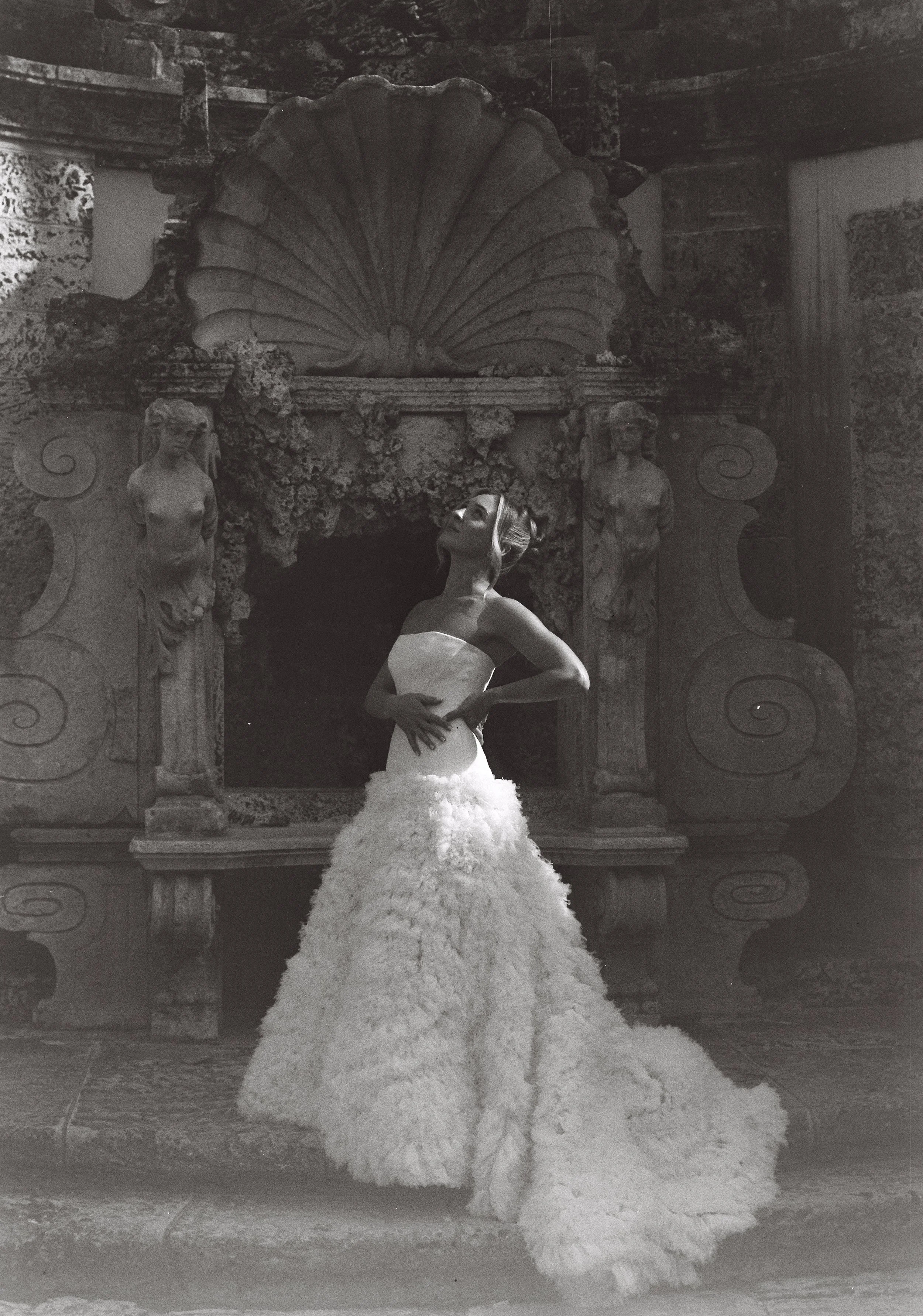 Bride posing in a dramatic textured wedding gown in front of an ornate historic stone fountain at Vizcaya Museum and Gardens in Miami.