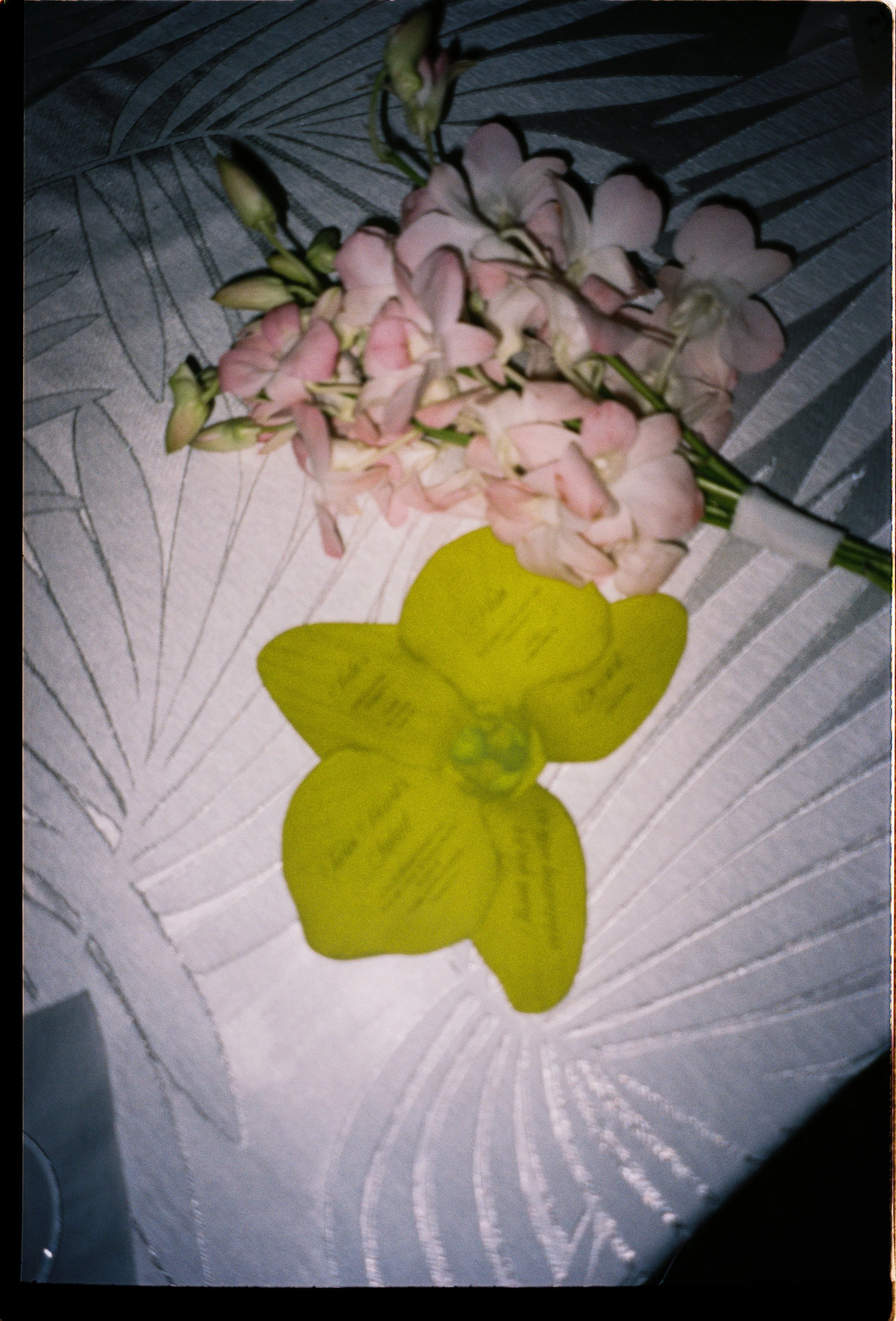 Orchid boutonniere resting on a patterned tablecloth beside a bright yellow flower-shaped escort card during a Vizcaya Museum and Gardens wedding reception in Miami.