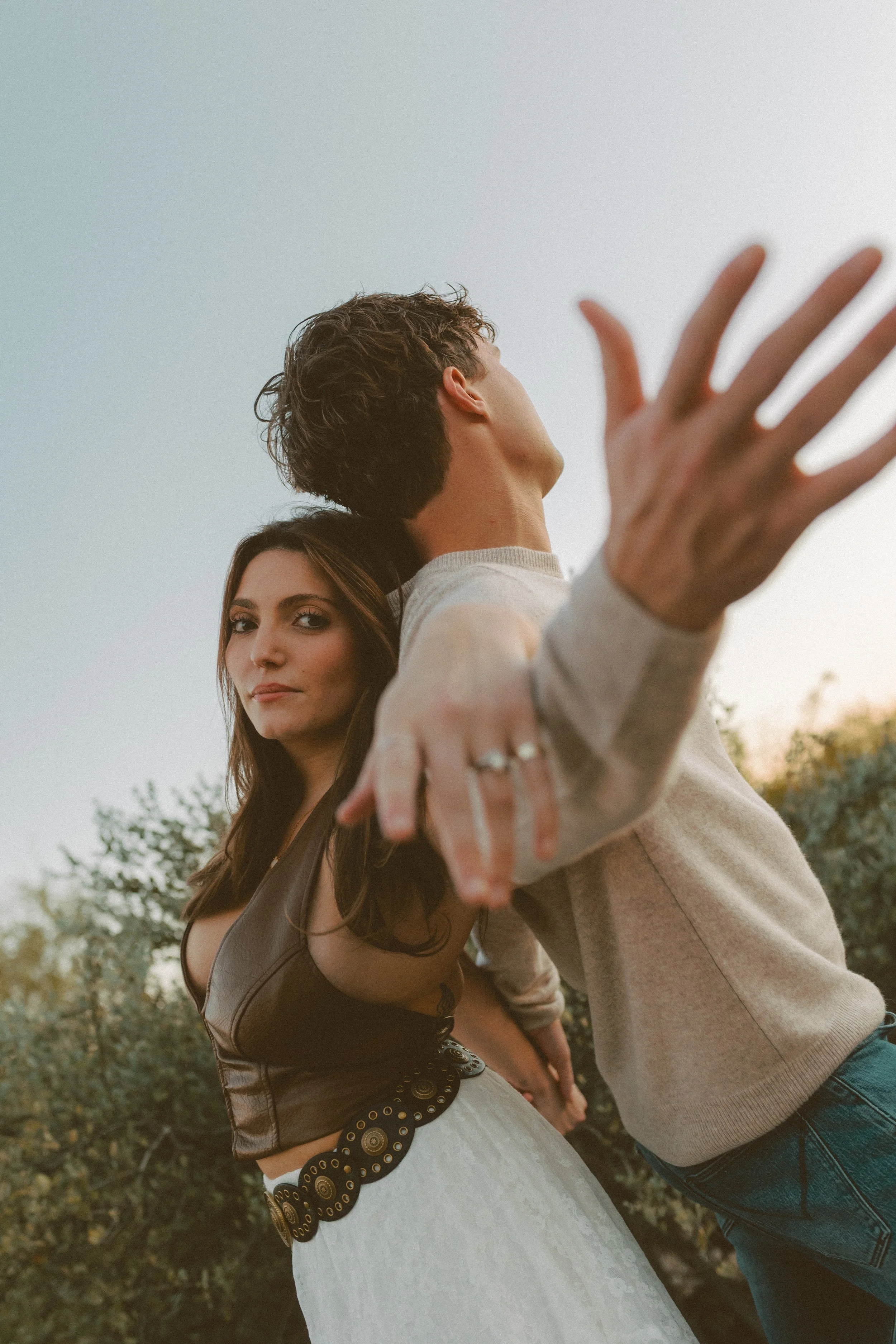 Creative close-up of a couple leaning back-to-back with arms extended, framed by soft desert light during a couple's photoshoot.