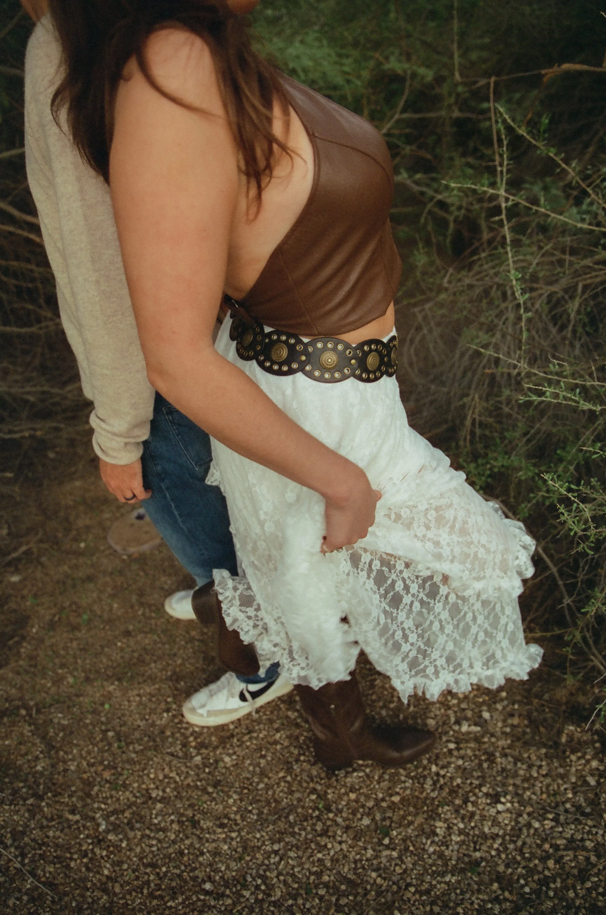 Detail shot of the bride’s lace skirt and western boots as she walks along a desert path beside her partner.