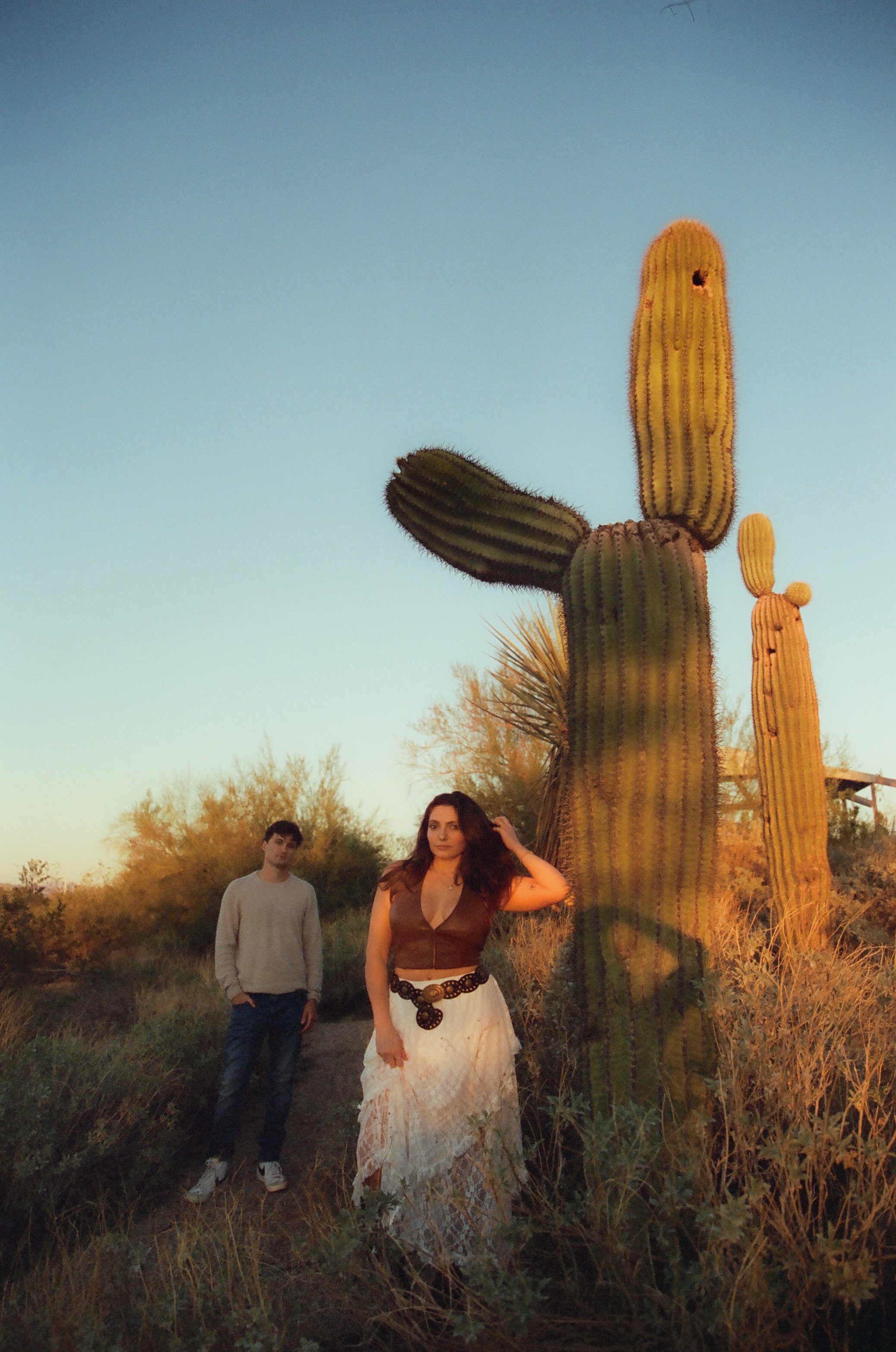 Couple posing near a towering saguaro cactus in warm golden light, capturing an editorial-style couple's photoshoot in the desert.