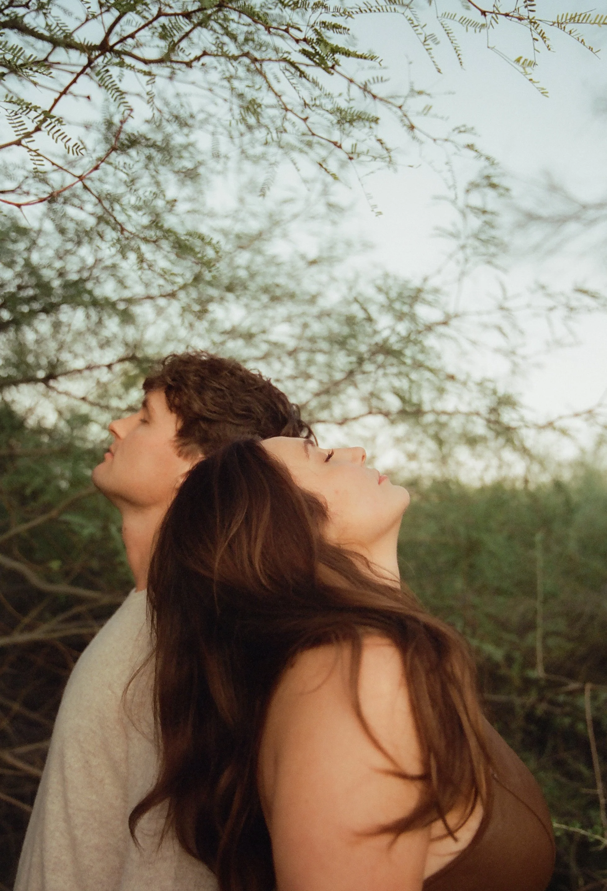 Intimate portrait of a couple leaning back against each other beneath delicate desert branches, eyes closed in a quiet moment.