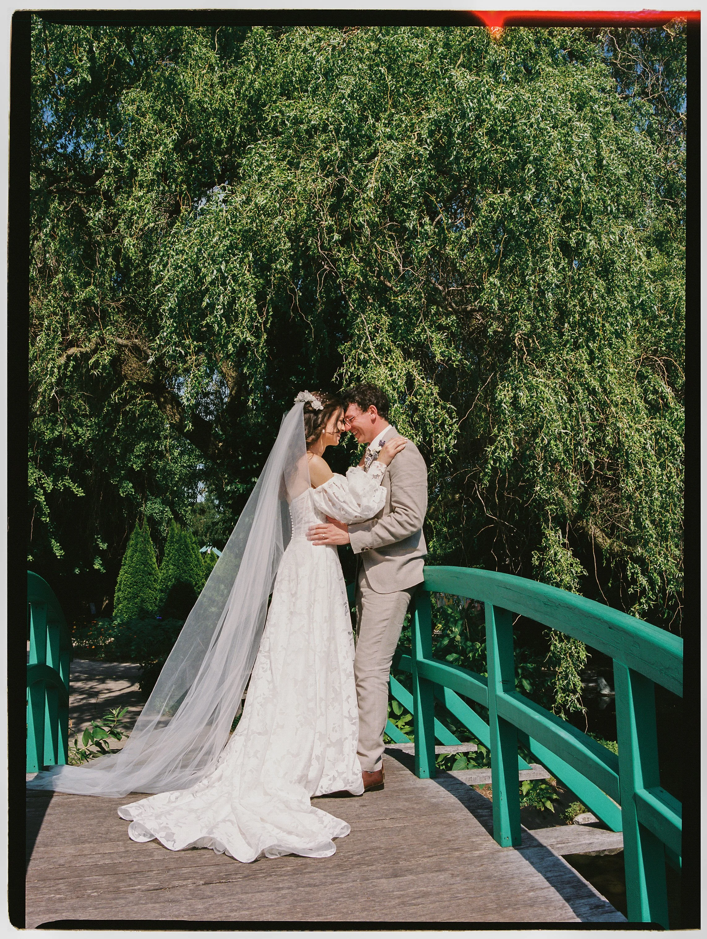 Bride and groom embracing on a green bridge surrounded by lush trees during their outdoor wedding