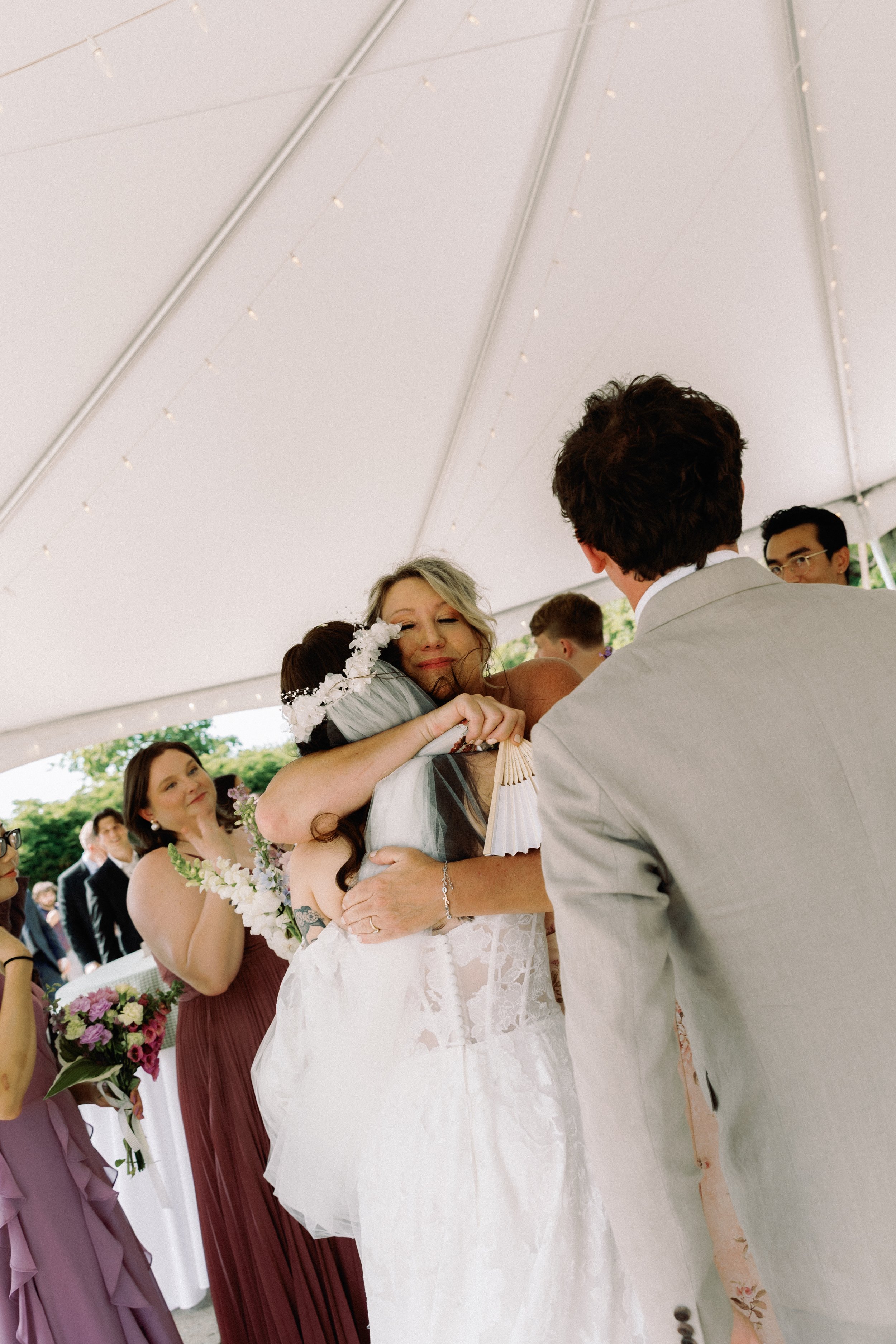 Bride hugging a family member under a reception tent, surrounded by emotional wedding moments captured in film wedding photography style
